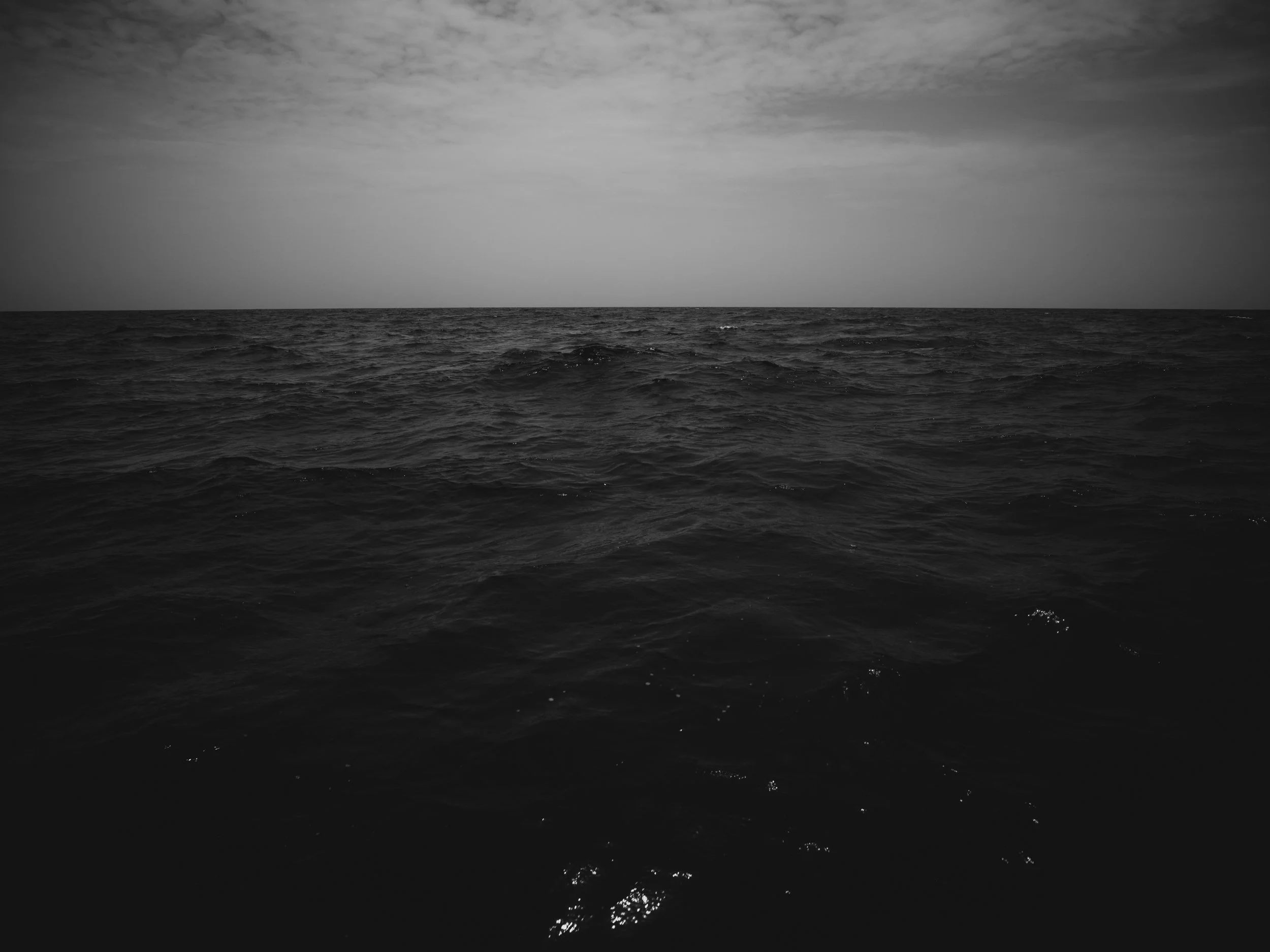 Black and white photograph of a vast ocean with small waves and a cloudy sky above.
