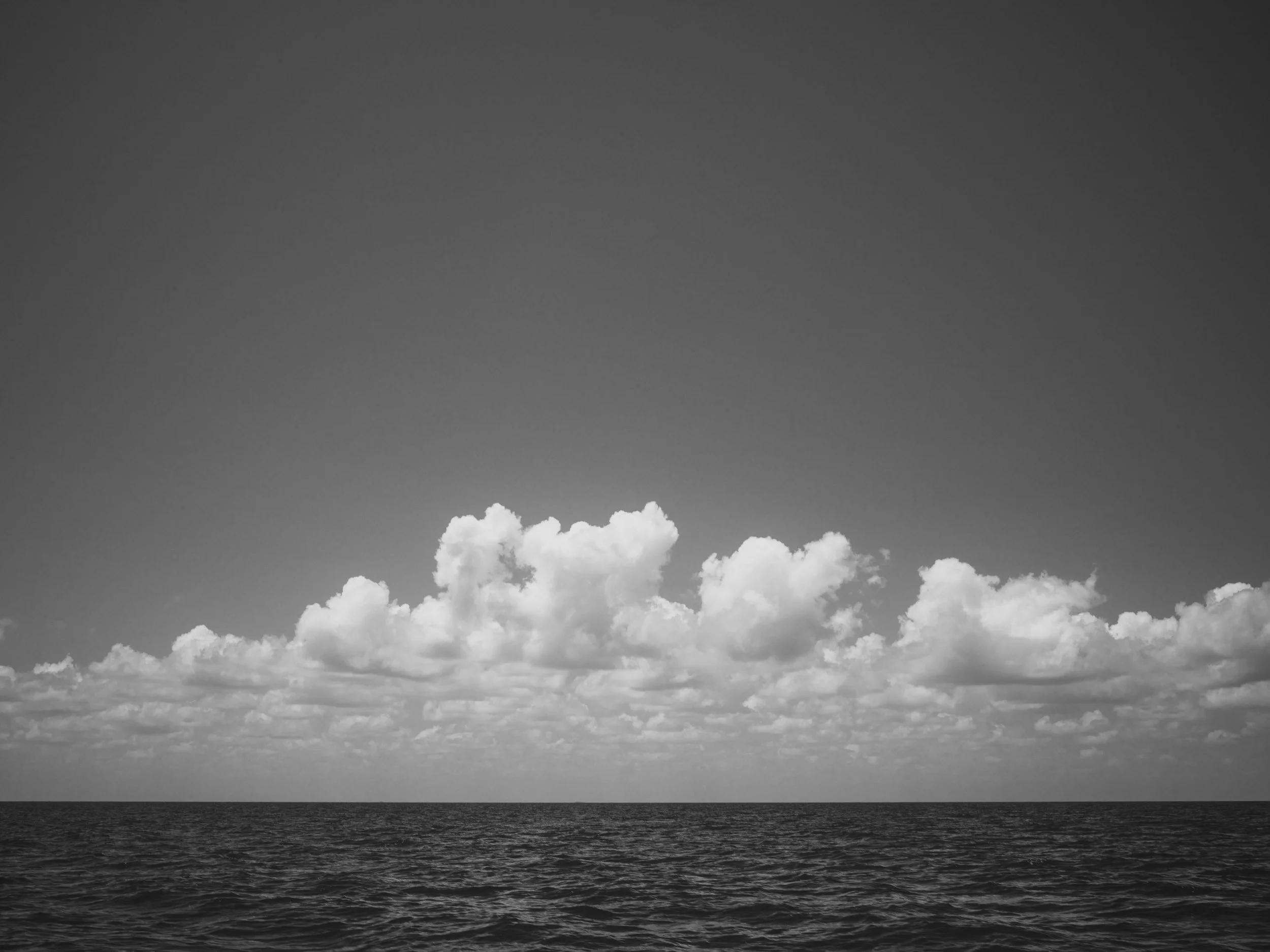 Black and white photograph of a cloudy sky over a body of water.