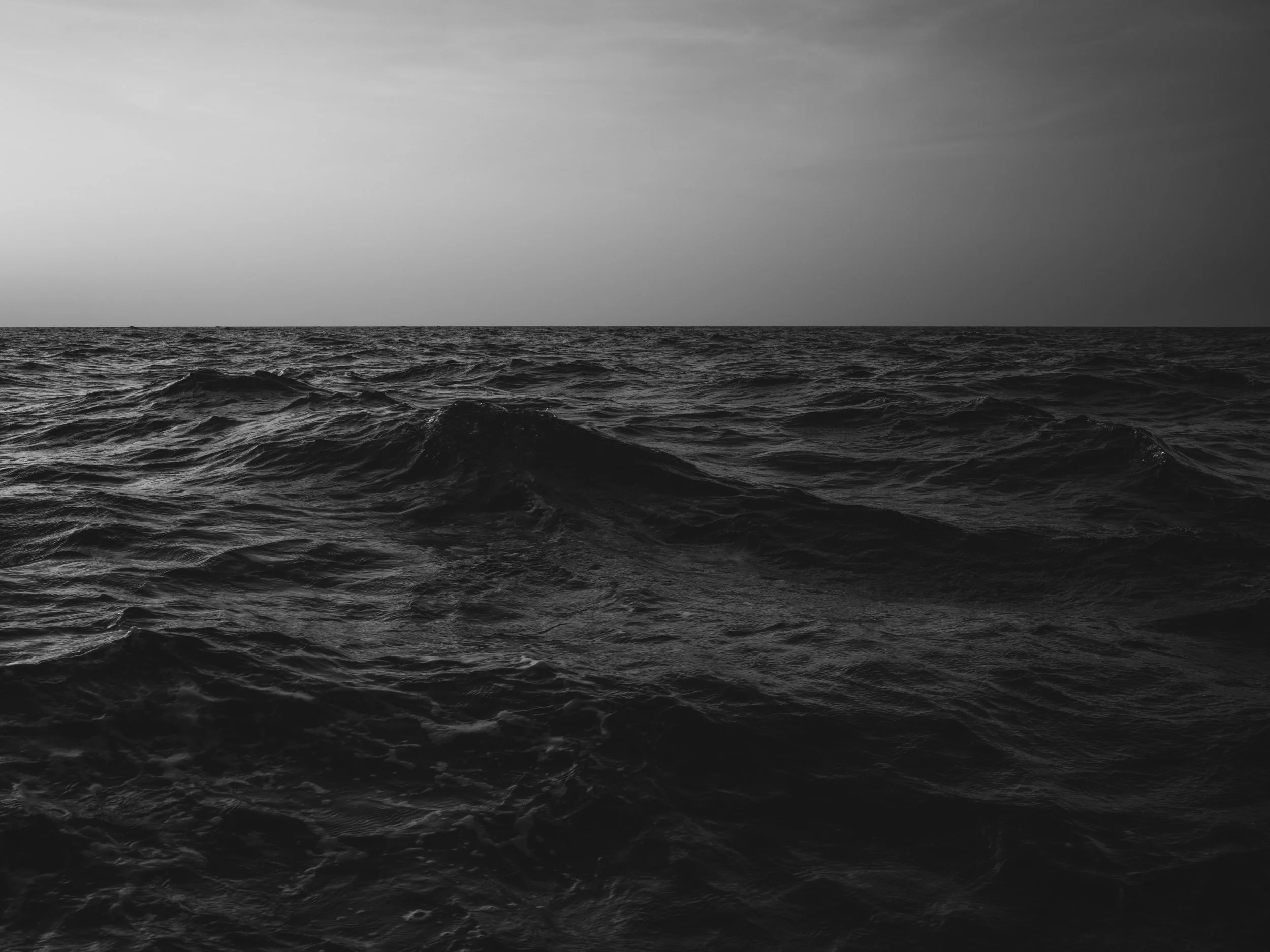 Black and white photograph of ocean waves and a cloudy sky at sea.