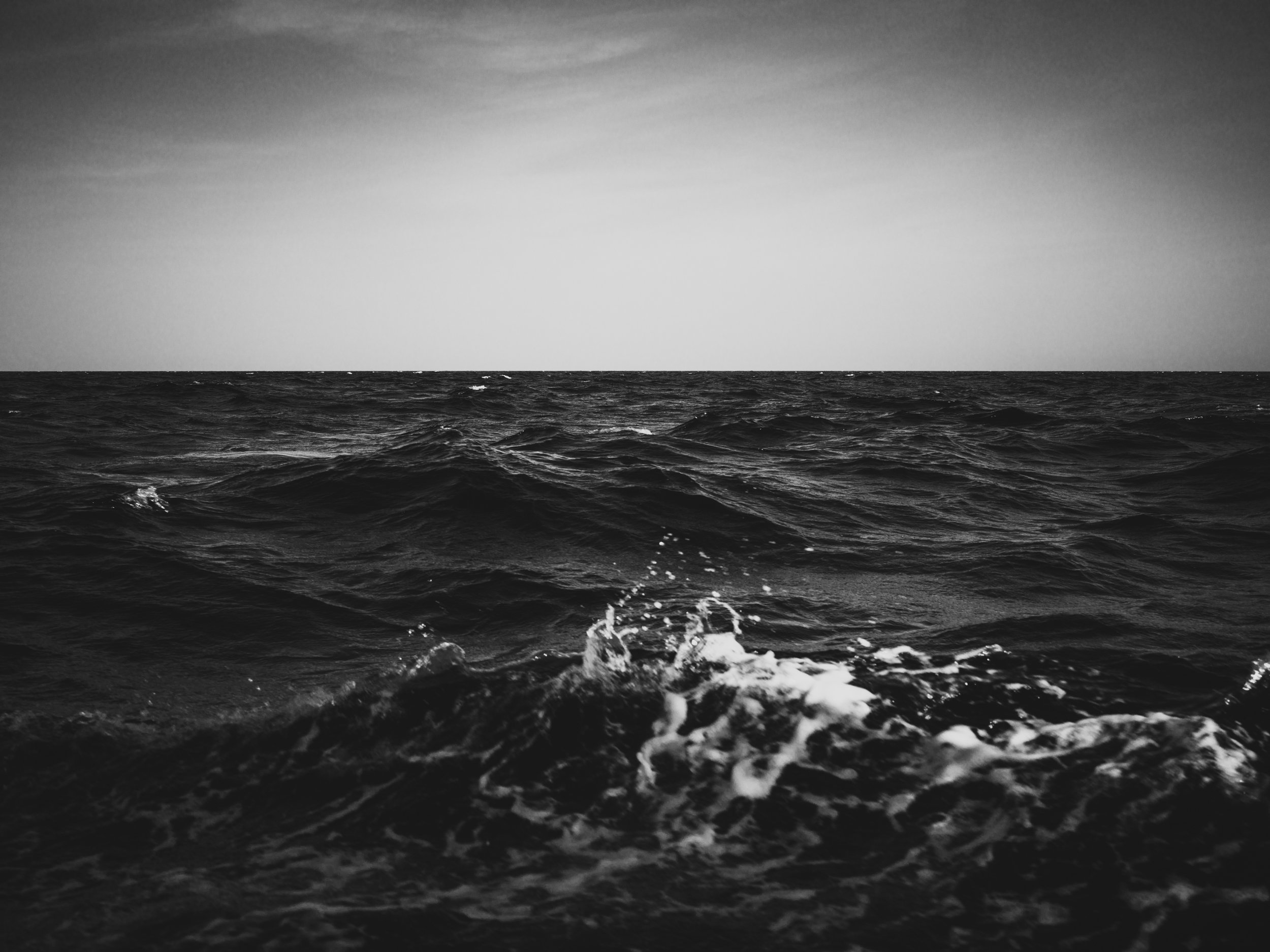 Black and white photo of ocean waves seen from a boat with the horizon in the distance, sky above.