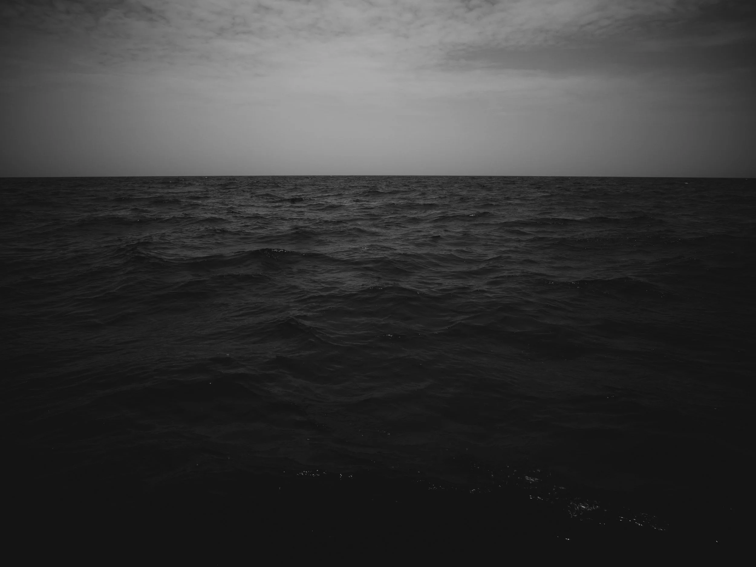 Black and white photo of the ocean with cloudy sky.
