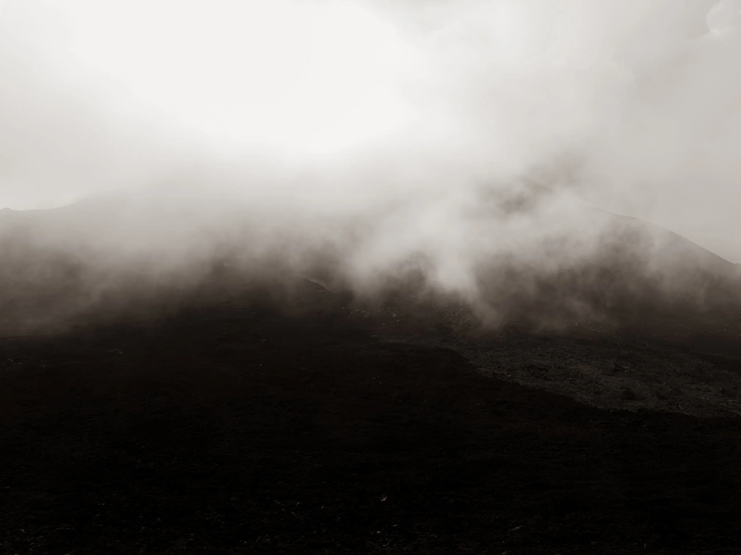 A dark, smoky landscape with mountains in the distance and a cloudy sky.