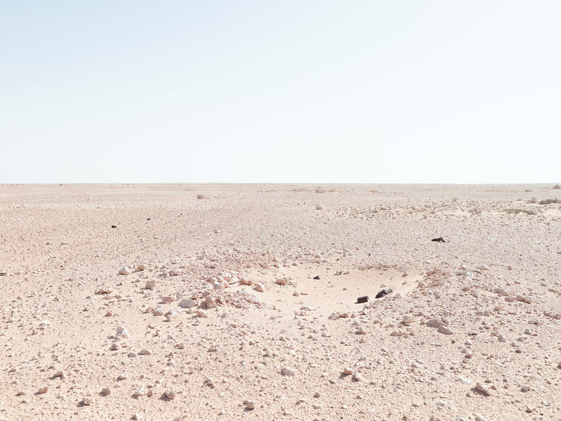 A wide, flat desert landscape with a clear sky and scattered rocks and debris on the sandy ground.