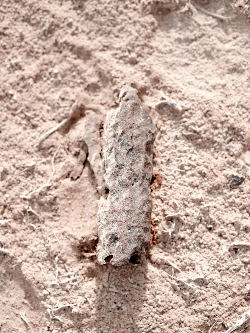 A rusted, weathered cigarette or similar-like object on dry, sandy ground.