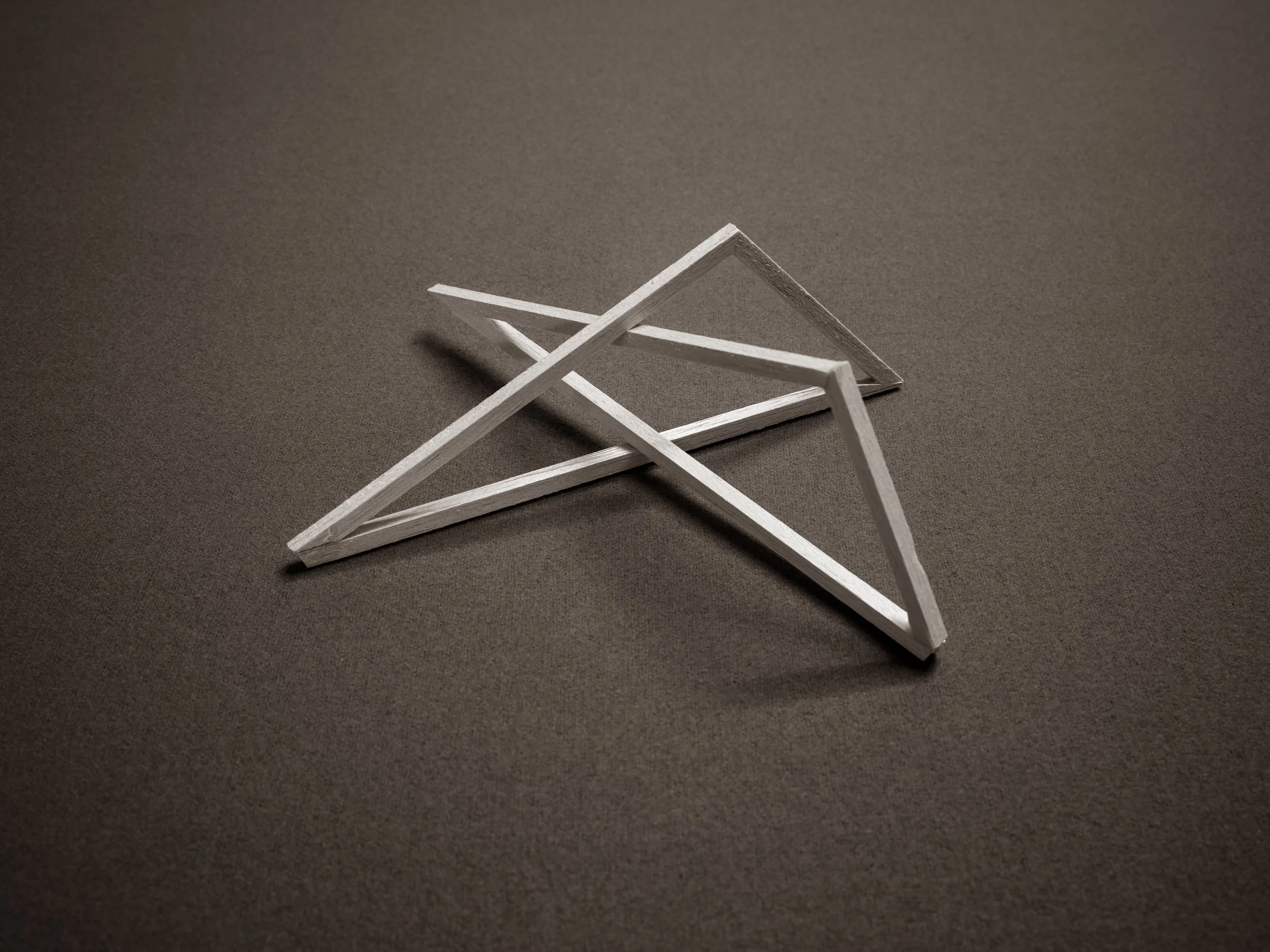 A small pyramid made of white wooden sticks on a dark surface.