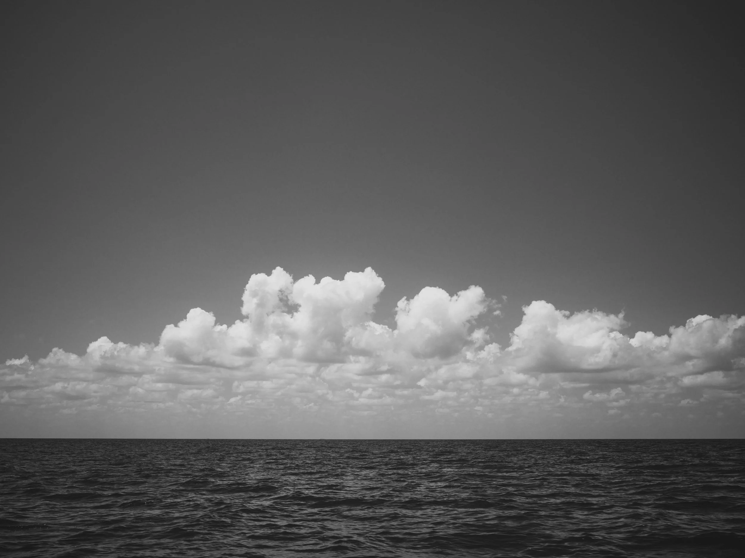 Black and white photo of an ocean with a horizon line, cloudy sky above.