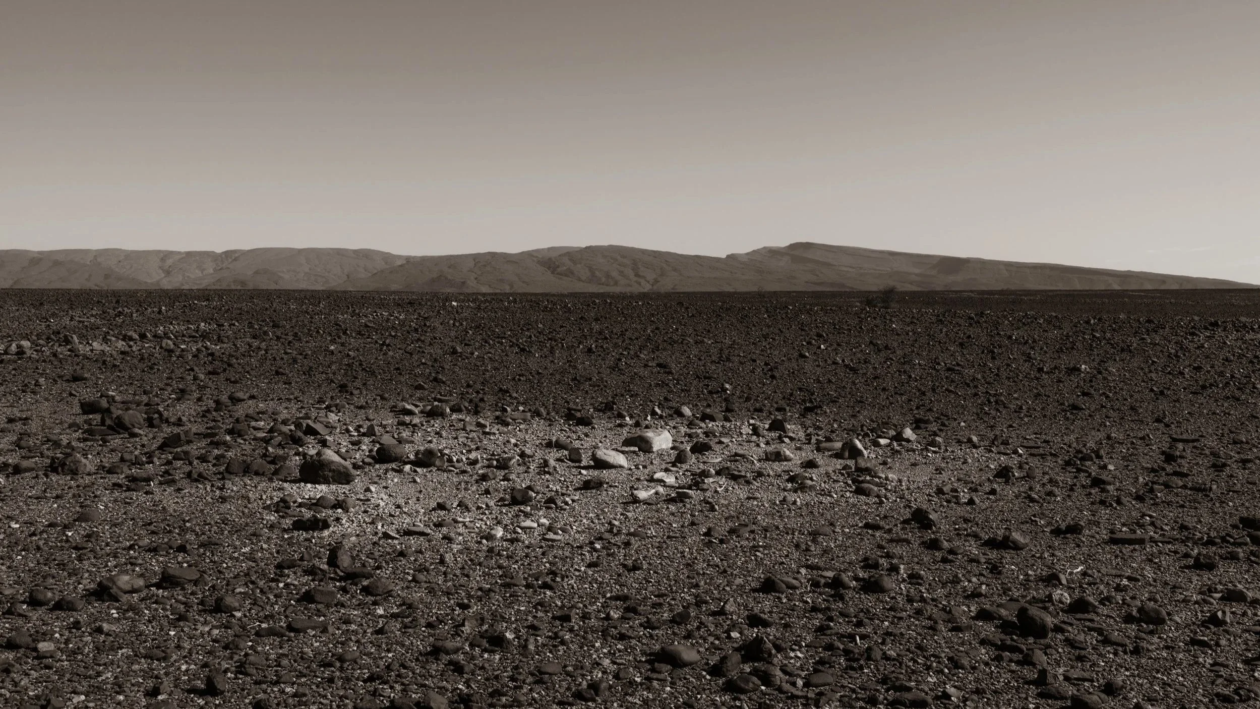 Desert landscape with rocky terrain and distant mountains under a clear sky.