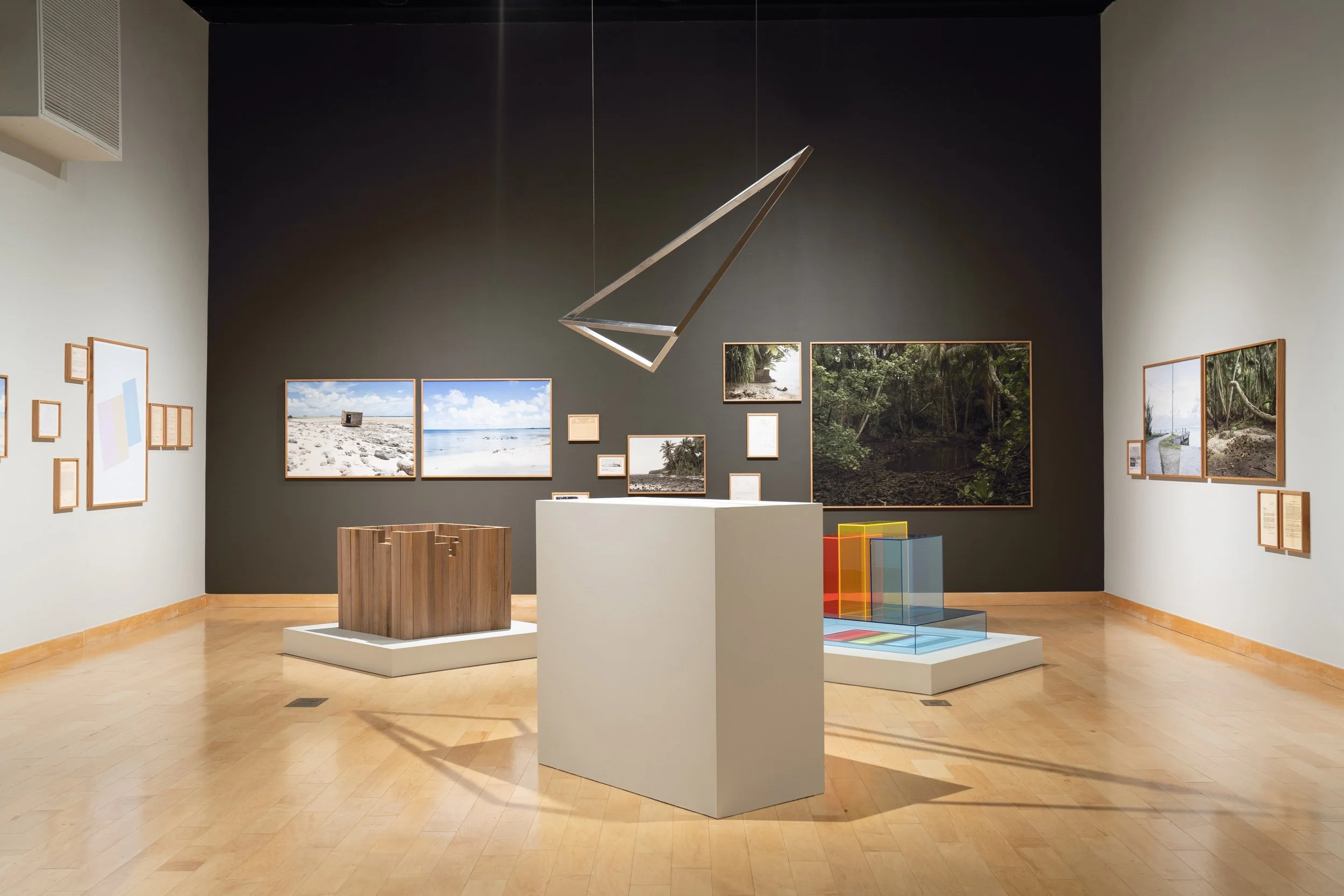Art gallery with framed photographs of nature scenes on the walls, a metallic geometric hanging sculpture, and several display stands including a small wooden one and a colorful transparent one.