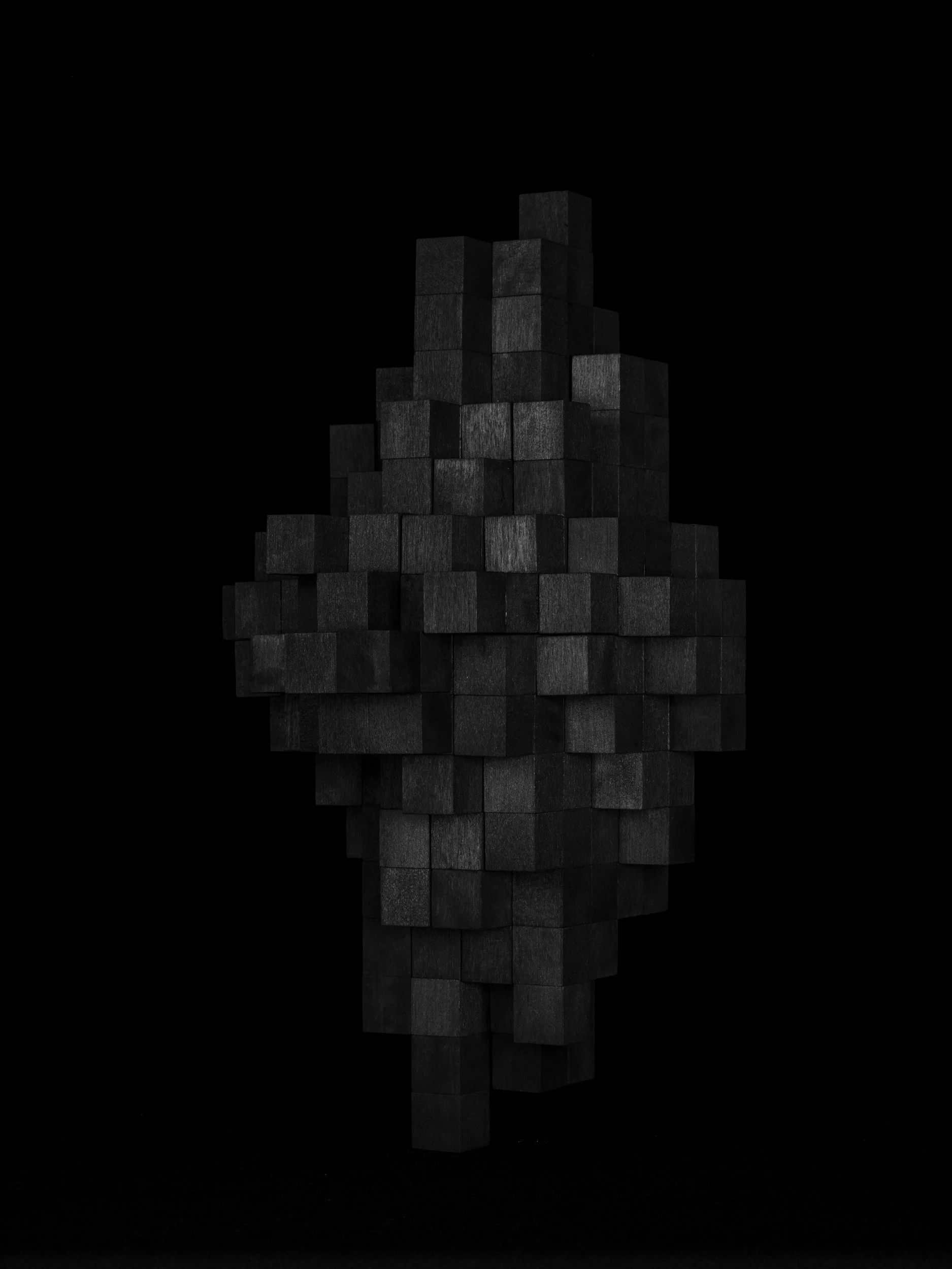 A modern sculpture simulating a pixelated, low resolution image of an asteroid—made of black cubes stacked in an abstract shape against a black background.