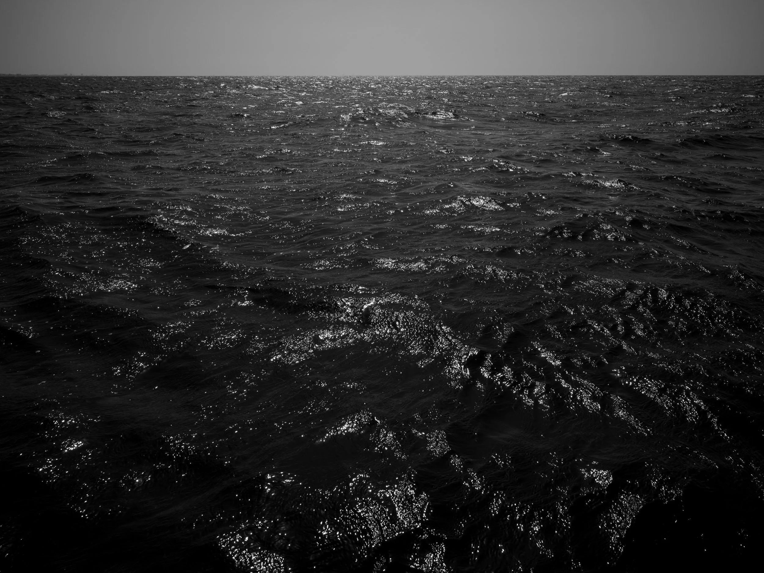 Black and white photo of ocean water with sunlight reflections on the surface.