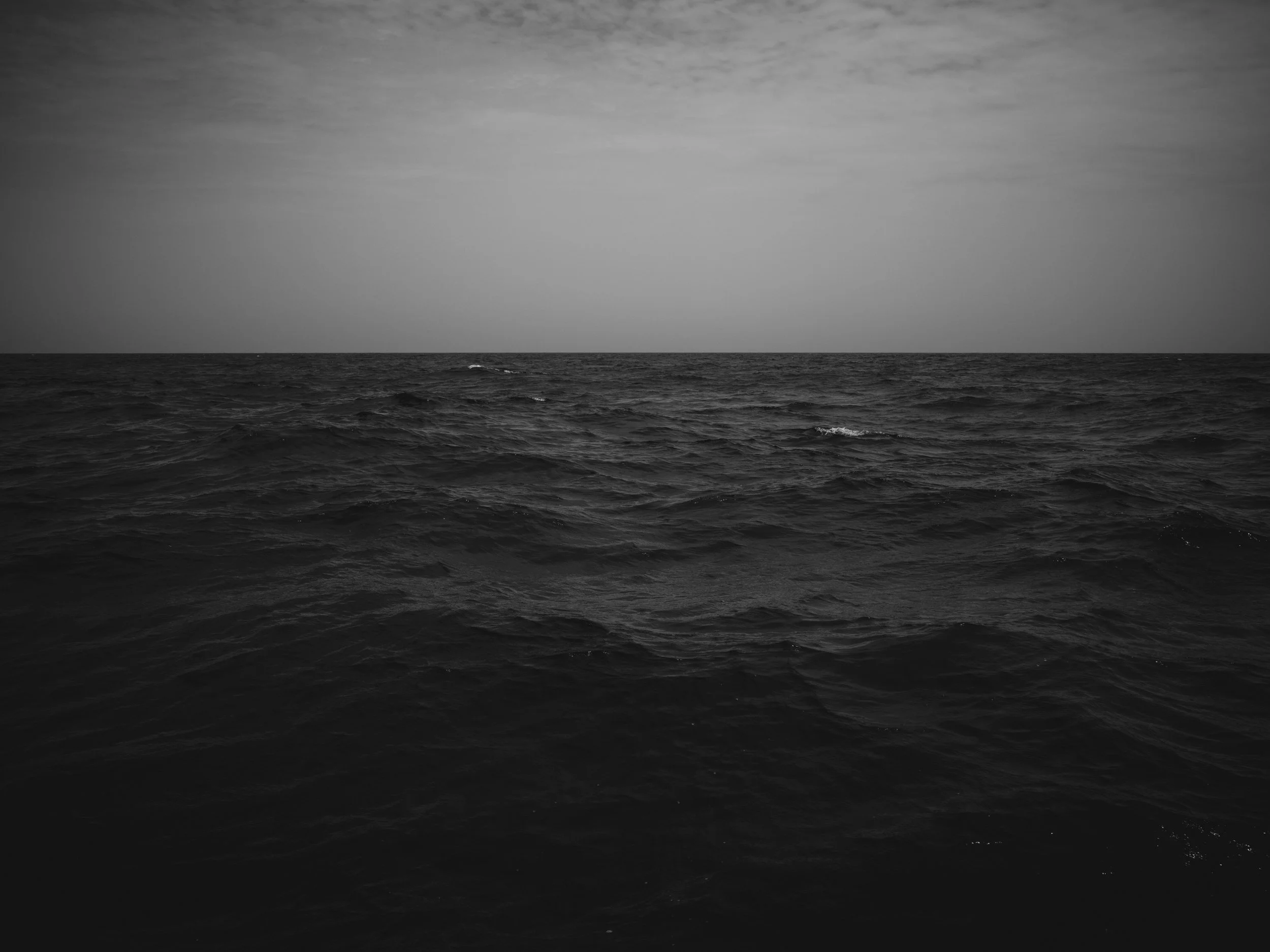 A black and white photograph of the ocean with choppy waves and a cloudy sky.