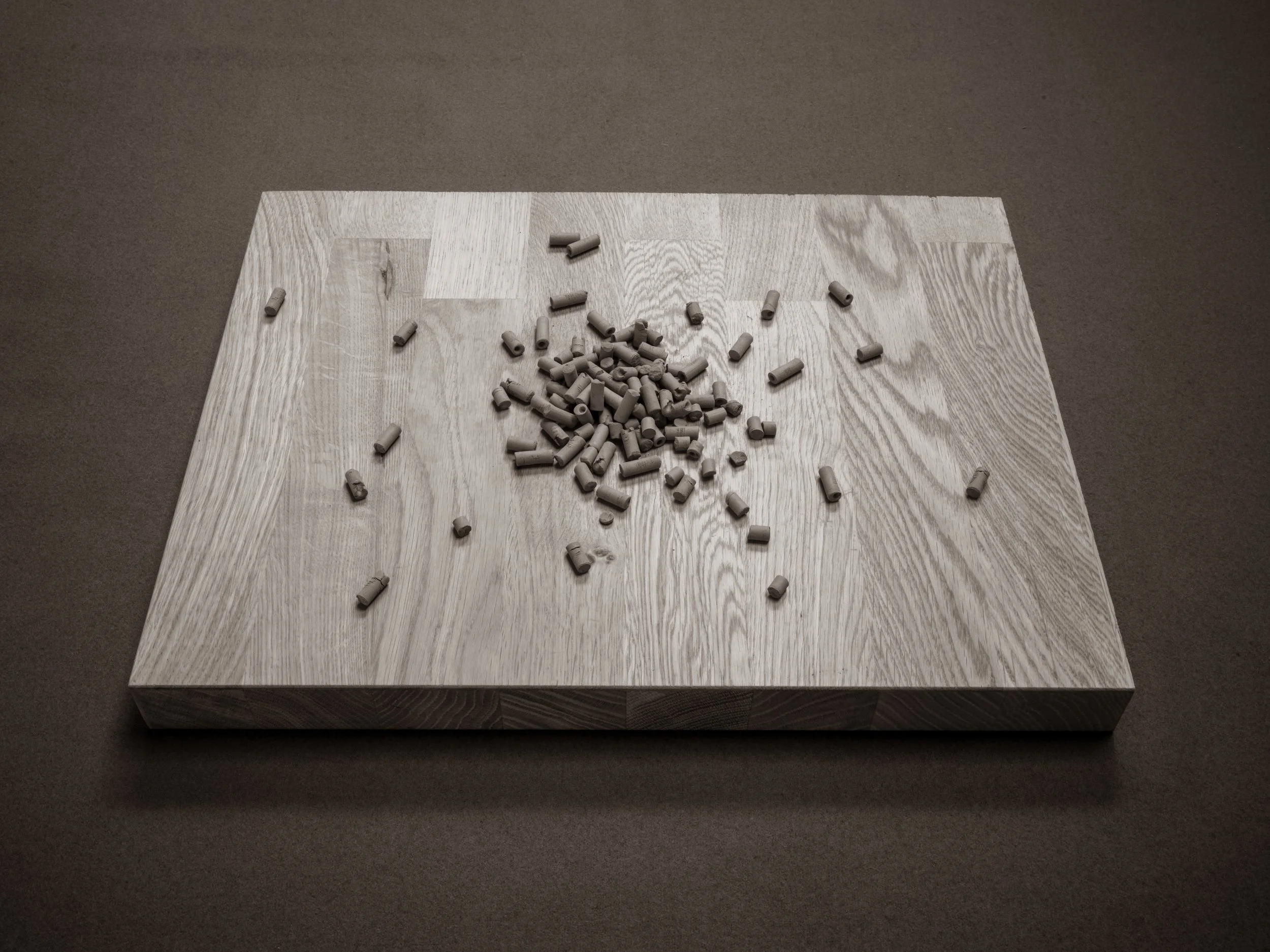 A wooden table with scattered gray chalk pieces on top, positioned on a brown carpeted floor.