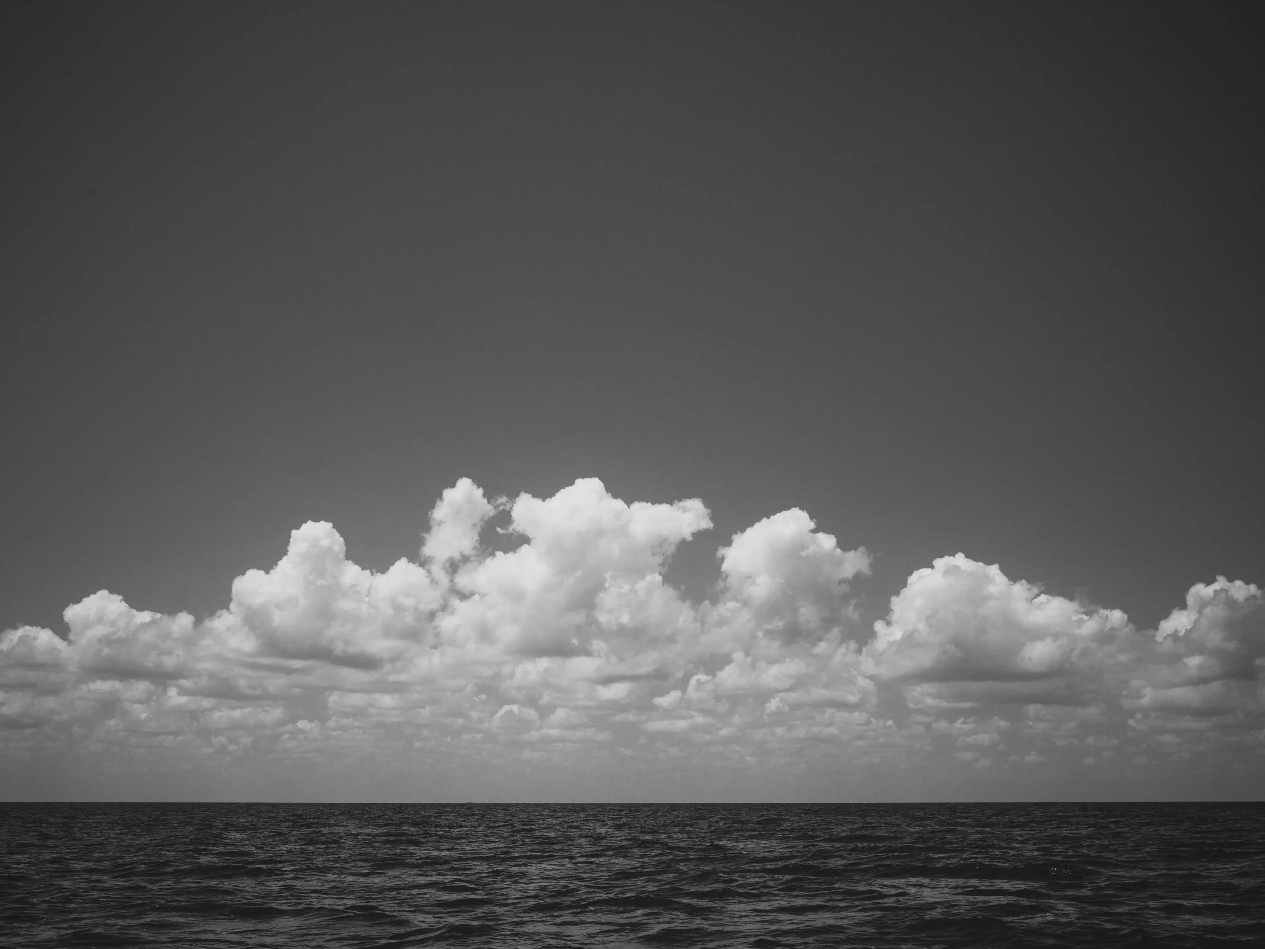 A black and white photo of a calm ocean under a cloudy sky with scattered clouds.