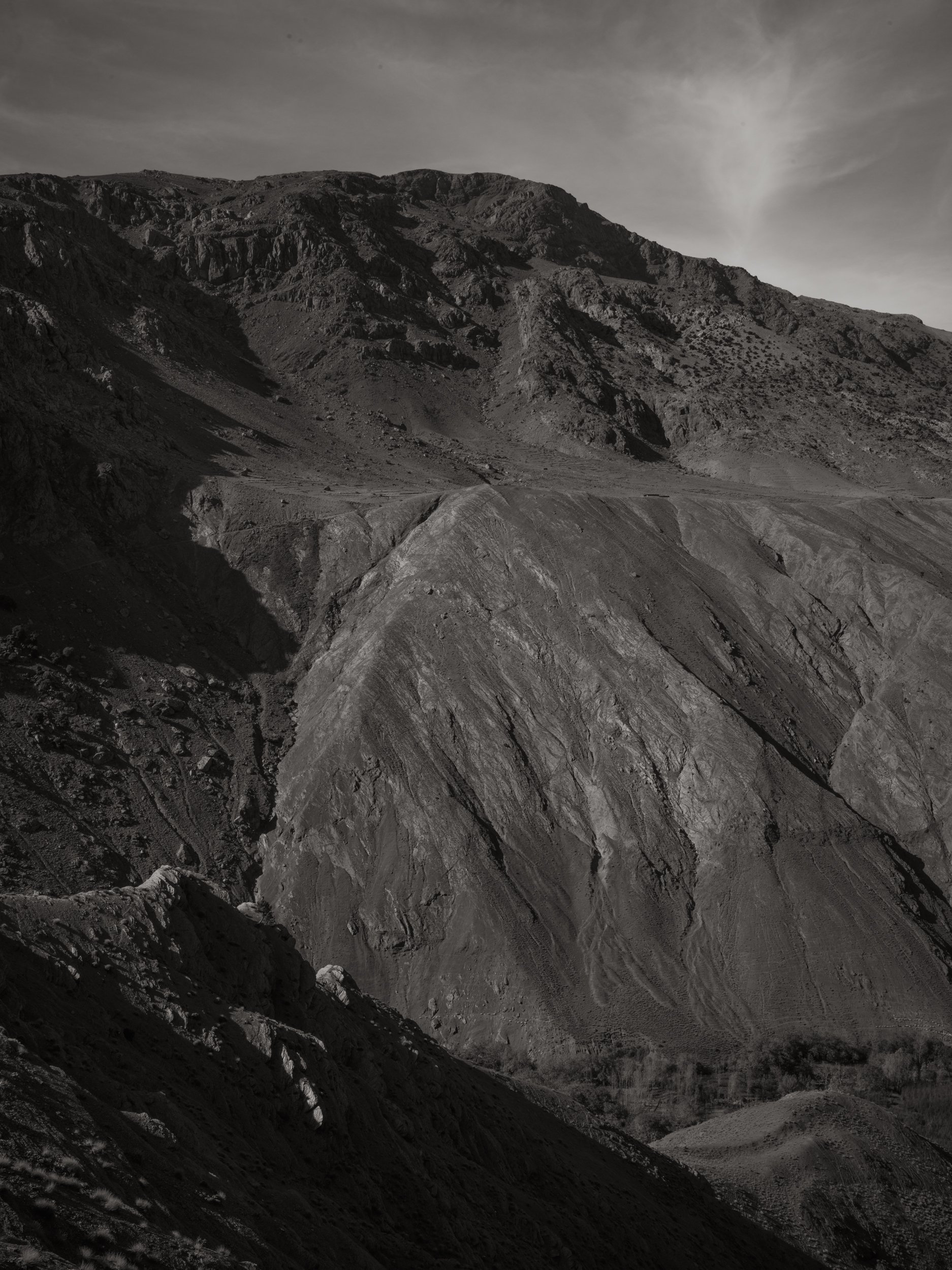Black and white photo of a mountain landscape with rocky slopes and a cloudy sky.
