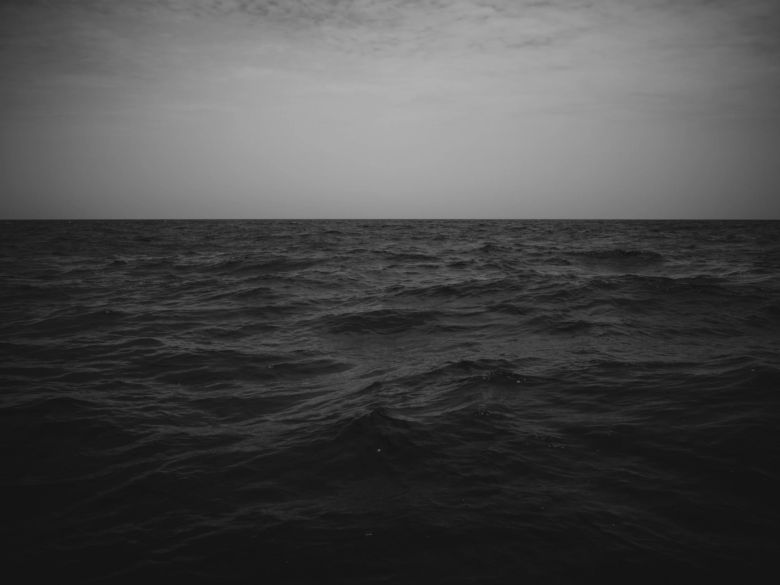Black and white photo of a calm ocean with a cloudy sky overhead.