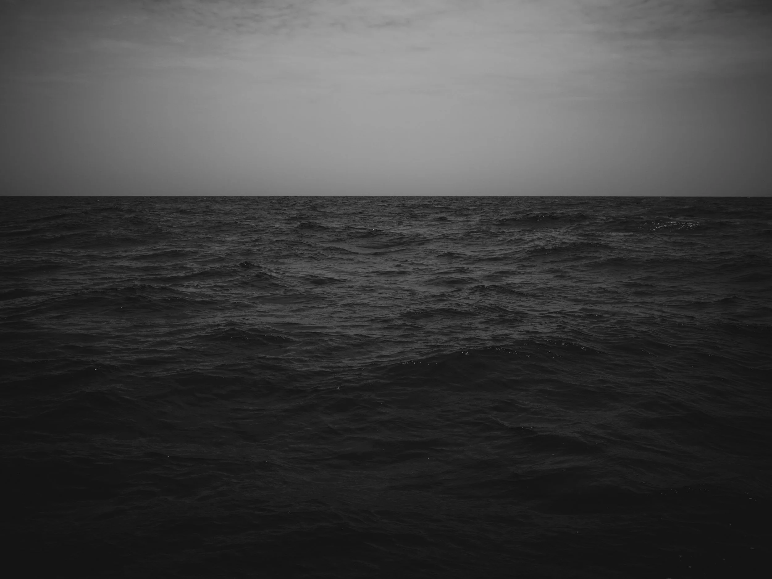 Black and white photo of an ocean with small waves and a cloudy sky.