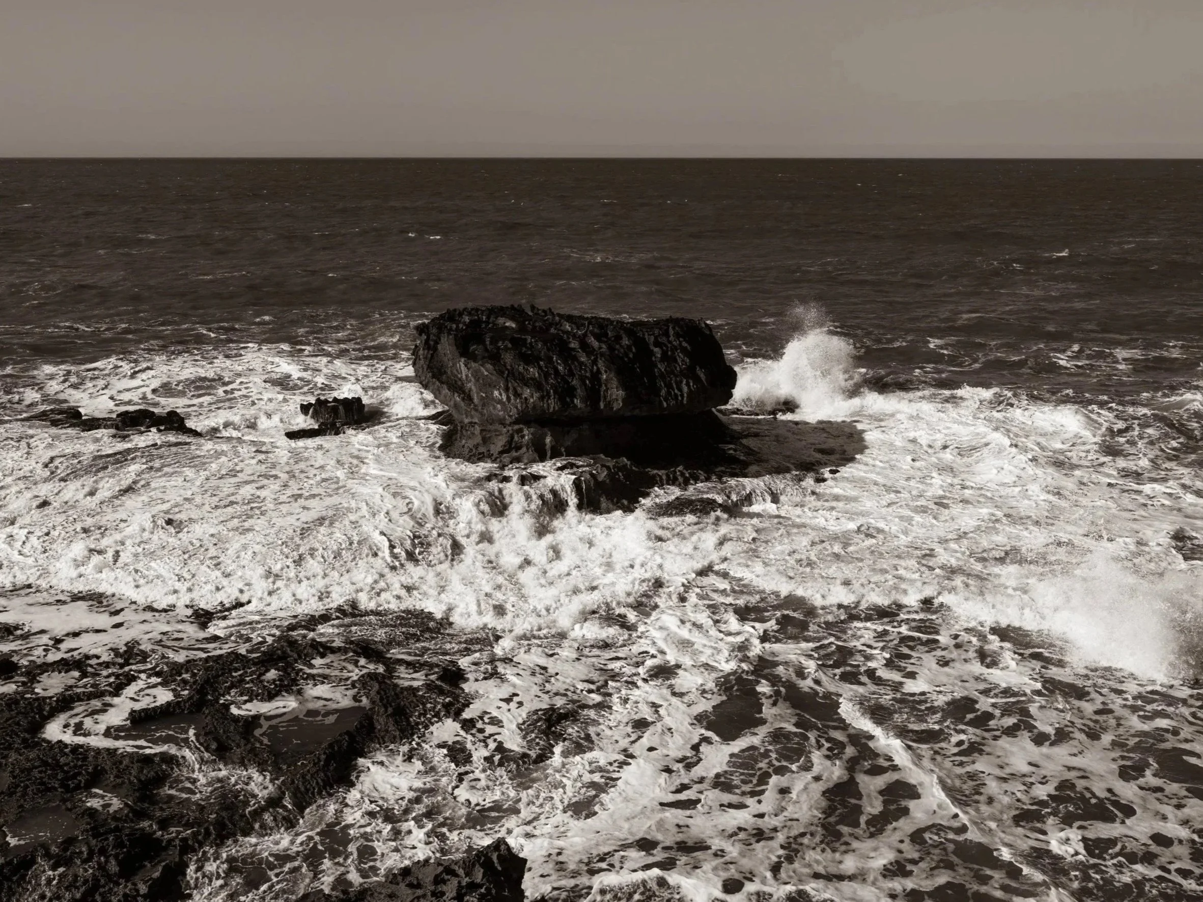 Ocean waves crashing against rocks on a gray overcast day.