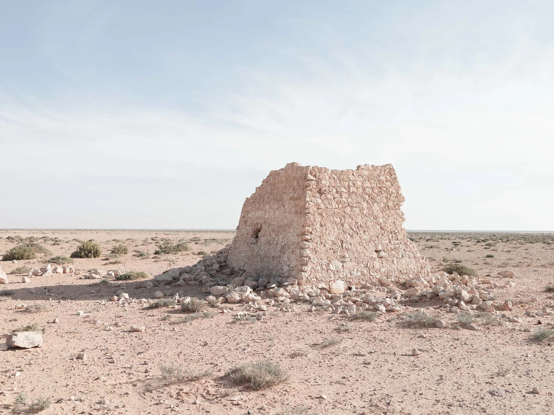 A stone structure in a desert landscape with sparse vegetation, under a mostly clear sky.