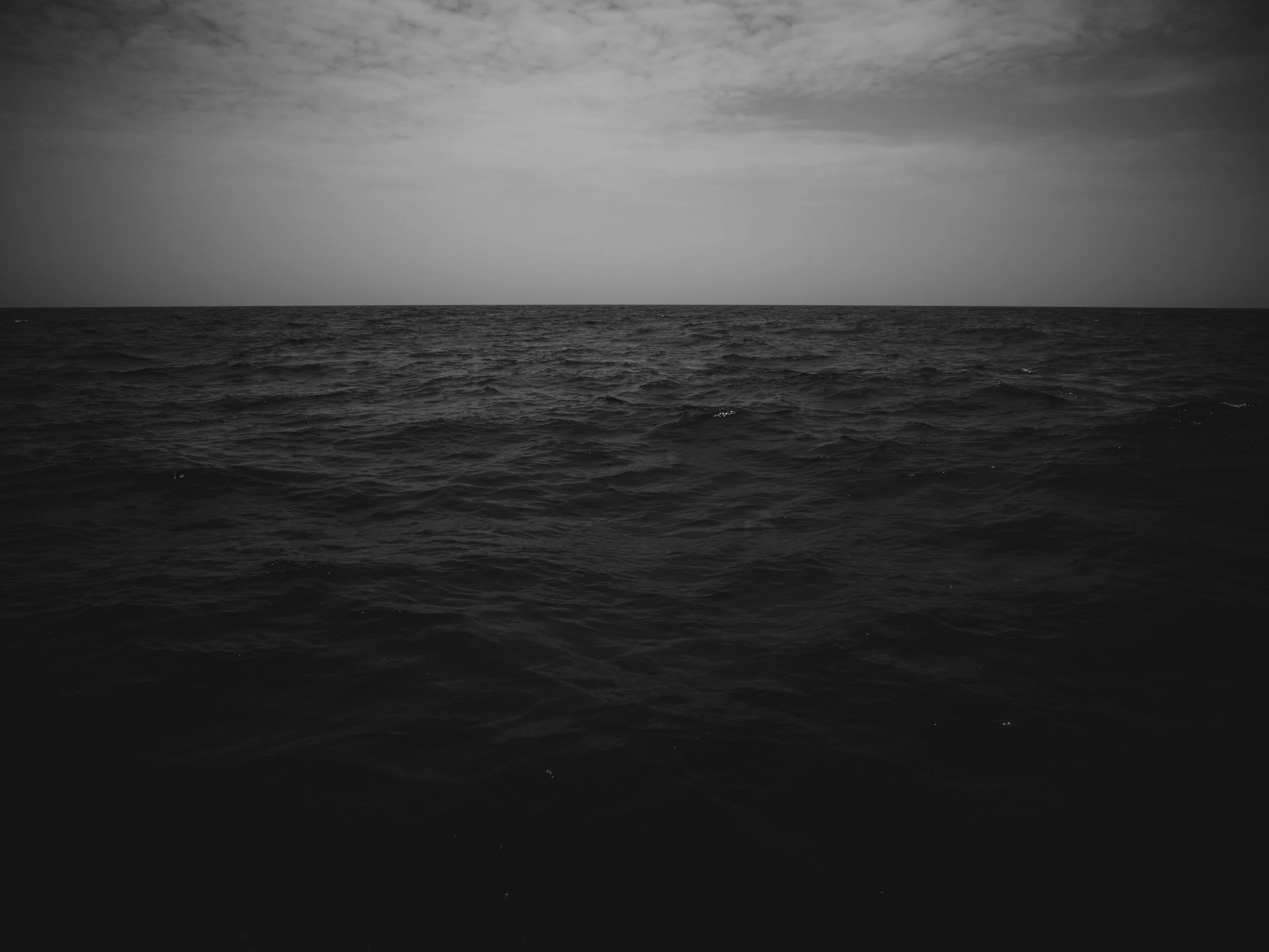 Black and white photograph of the ocean with a cloudy sky.
