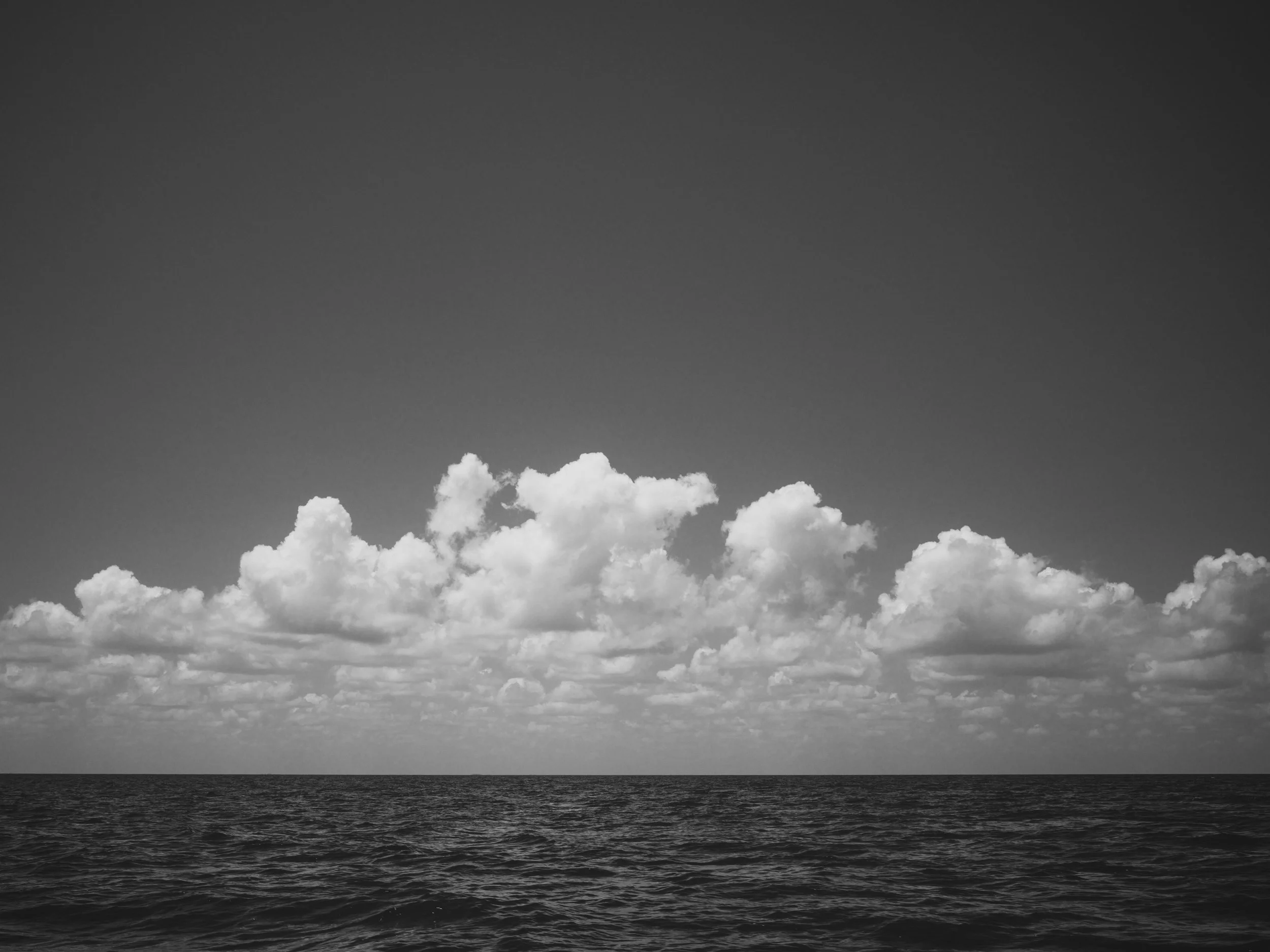 A black and white photo of the ocean with cloudy skies overhead.