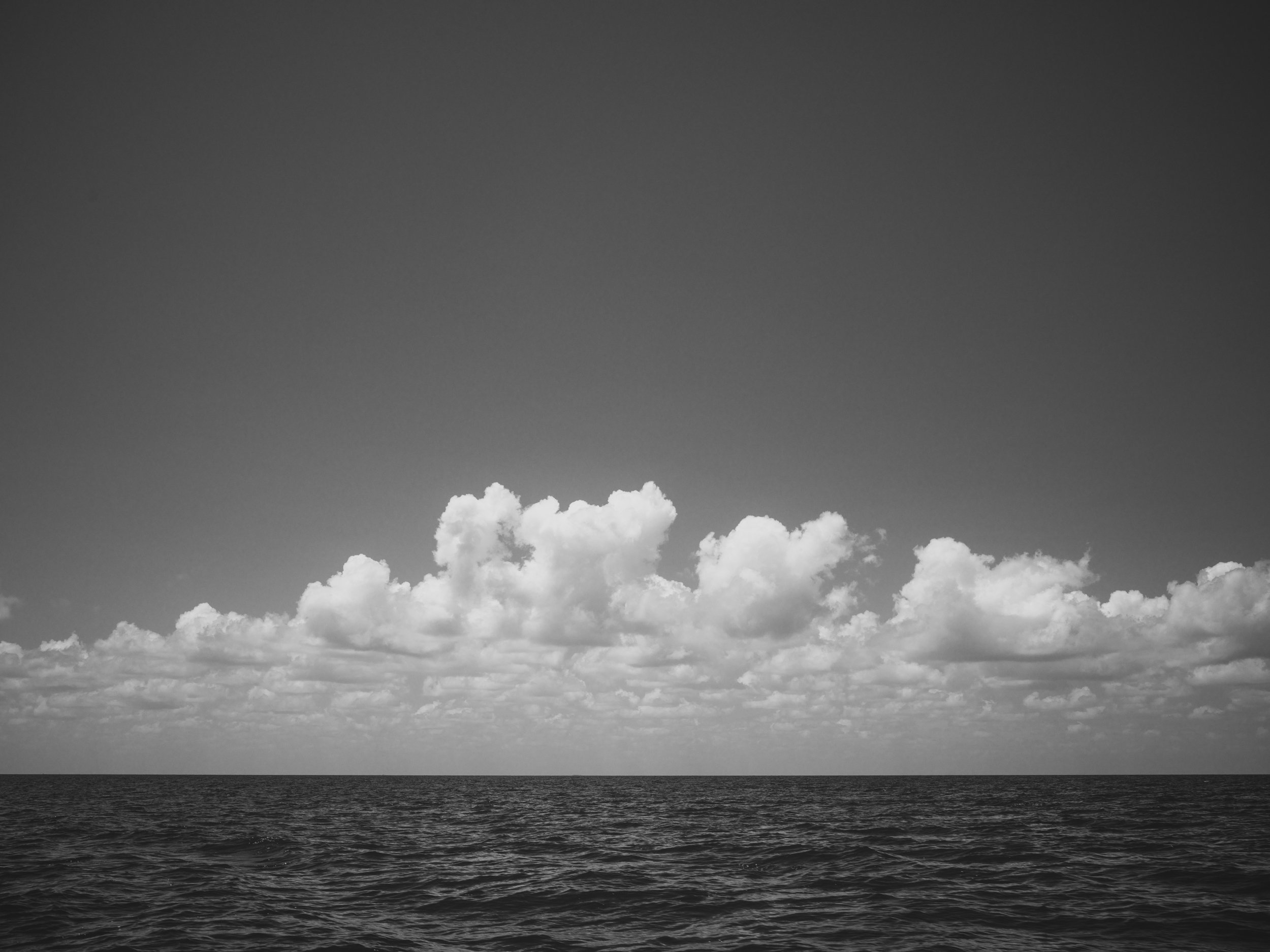 Black and white photograph of the ocean with clouds above.