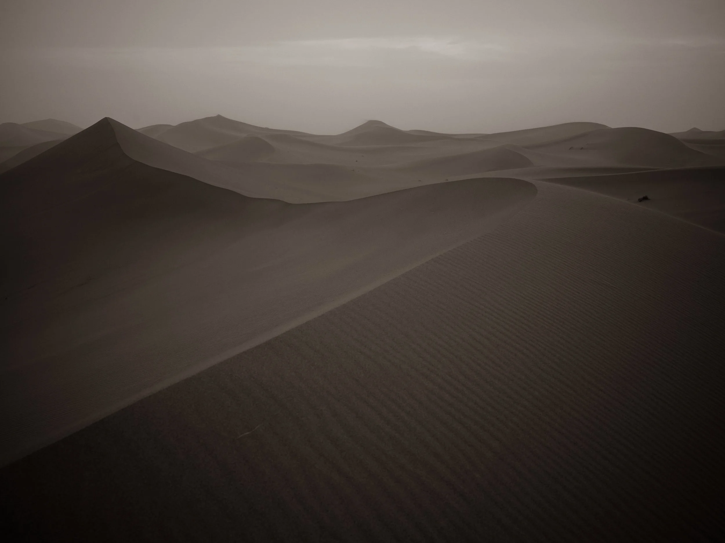 Dune landscape with sand dunes and cloudy sky, black and white photograph.