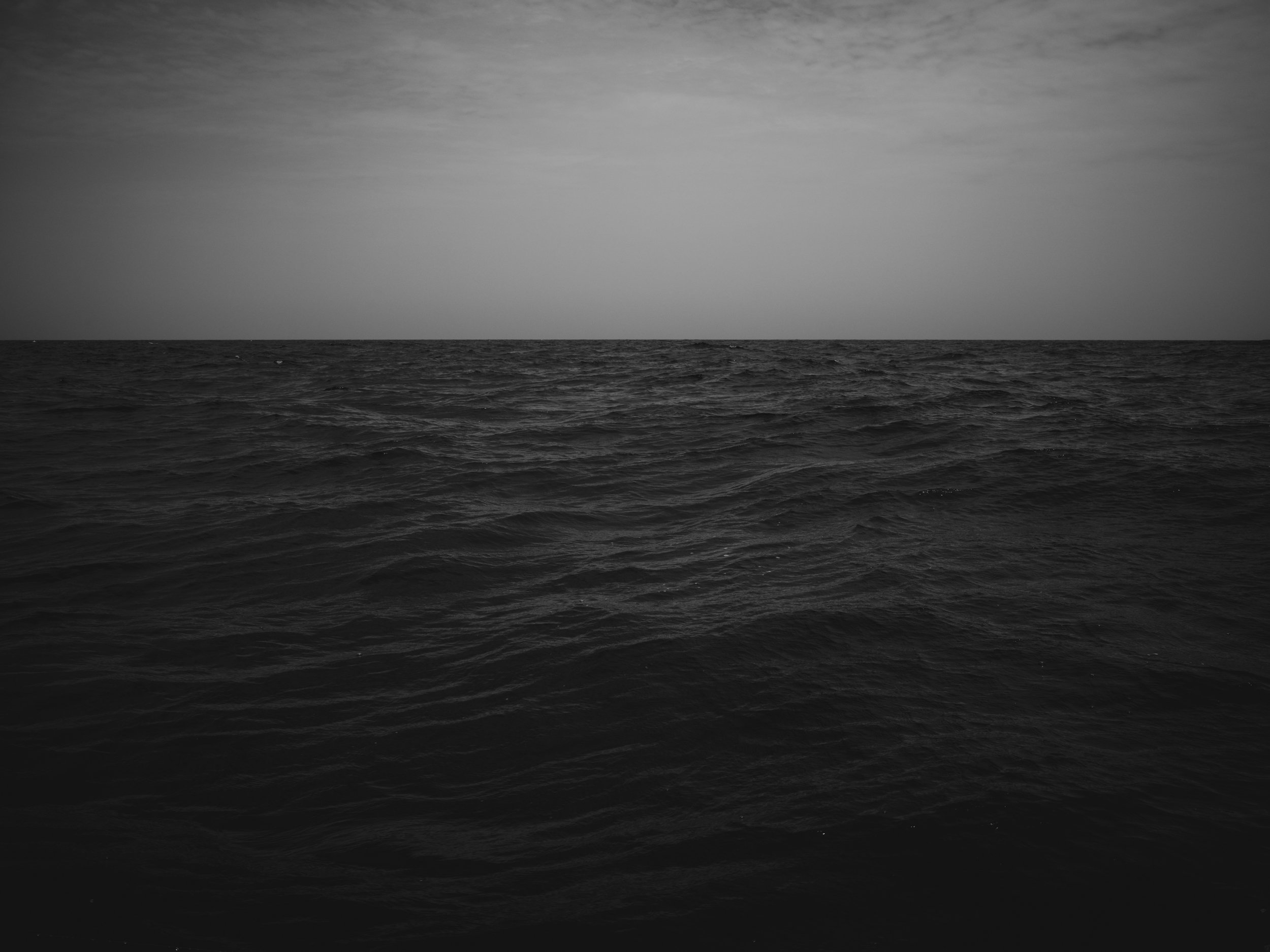 A black and white photo of the ocean with choppy waves under a cloudy sky.
