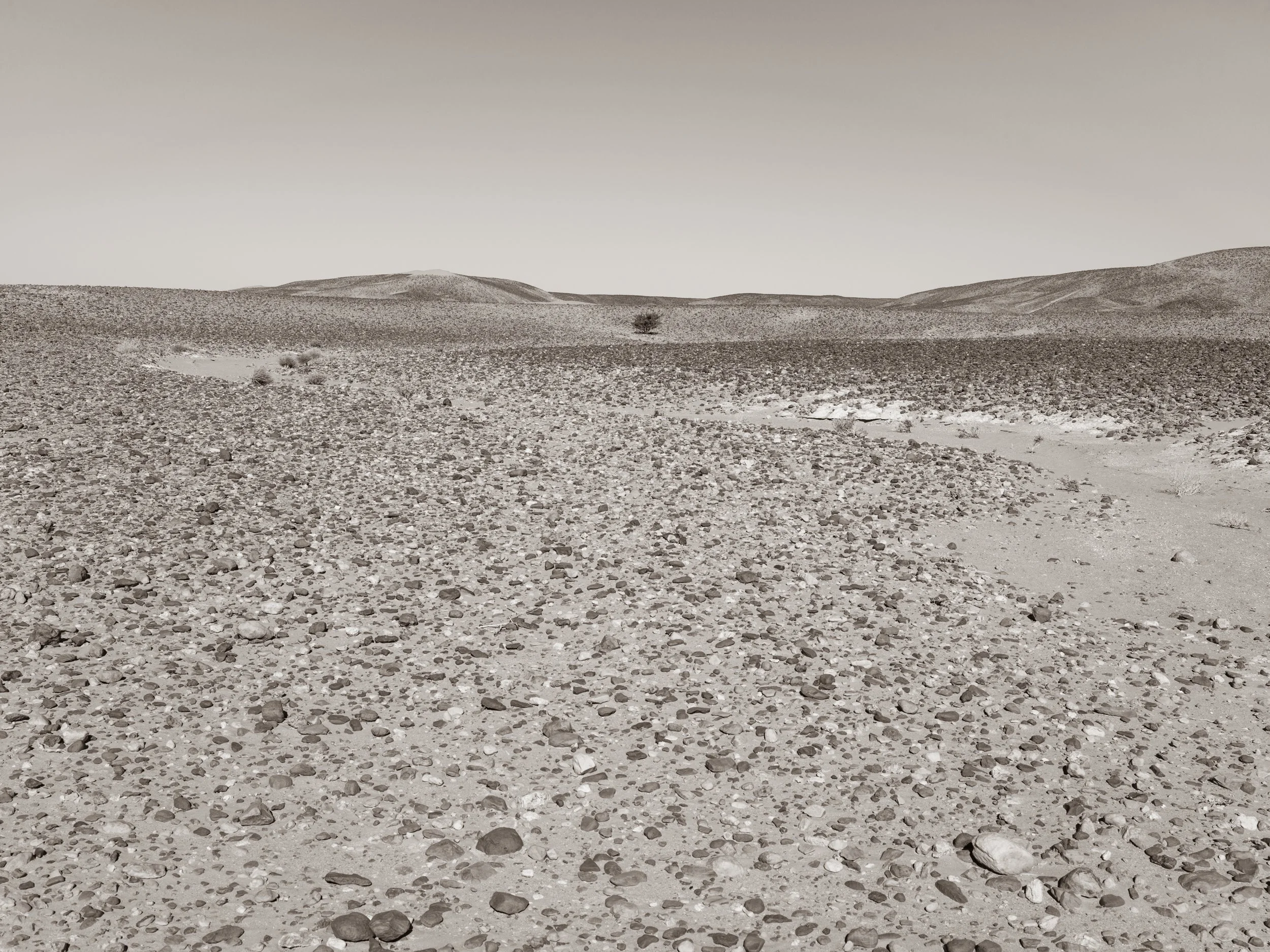 A barren desert landscape with rocky terrain and distant rolling hills under a clear sky.