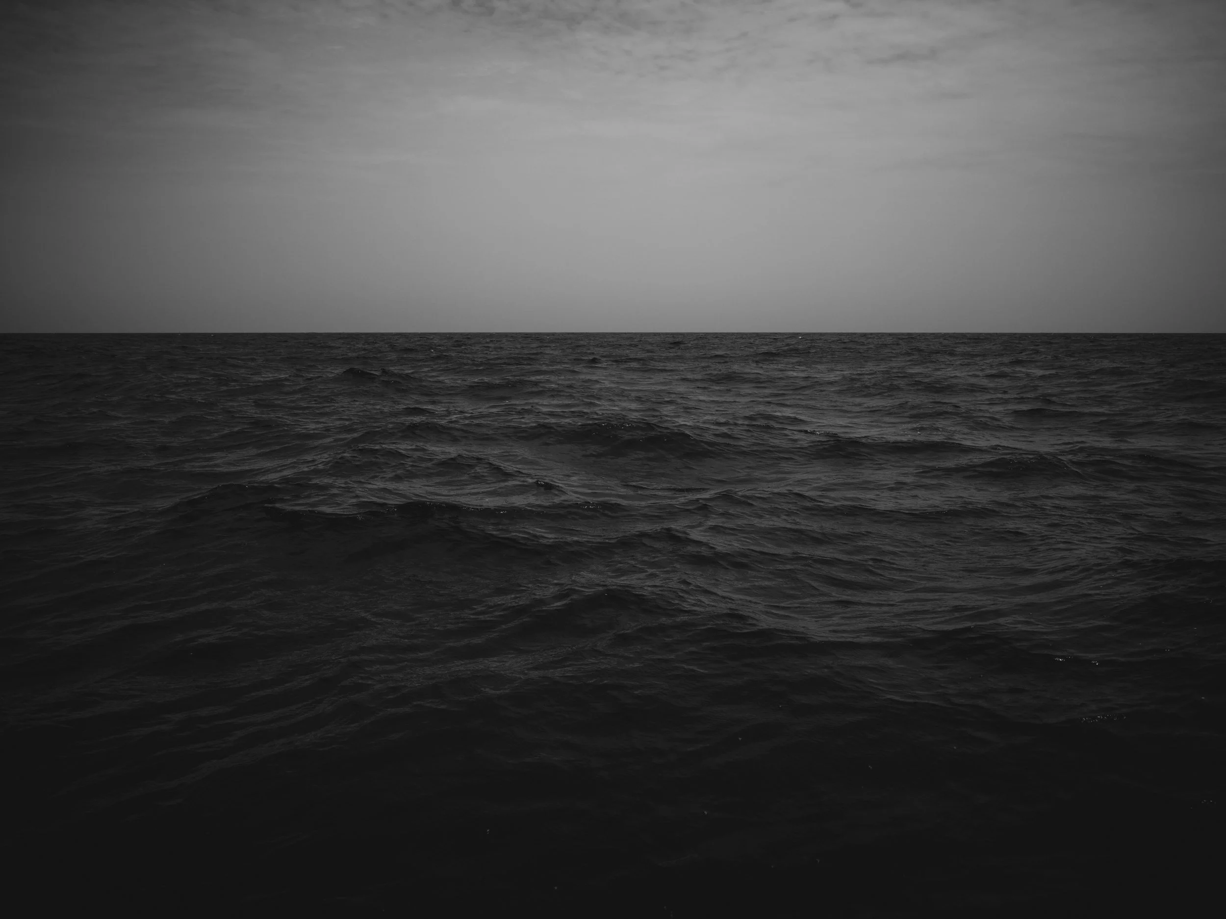 Black and white photograph of an ocean with large waves under a partially cloudy sky.