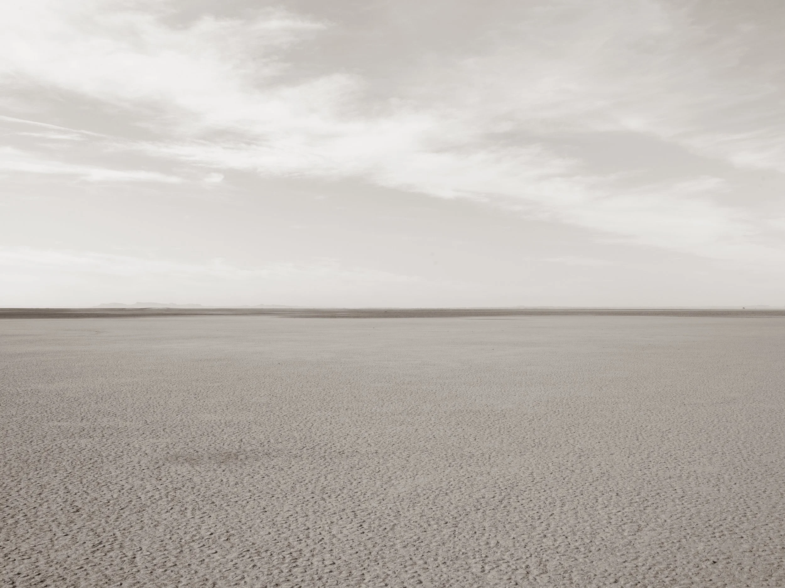 Dried salt flat landscape with textured ground and cloudy sky.