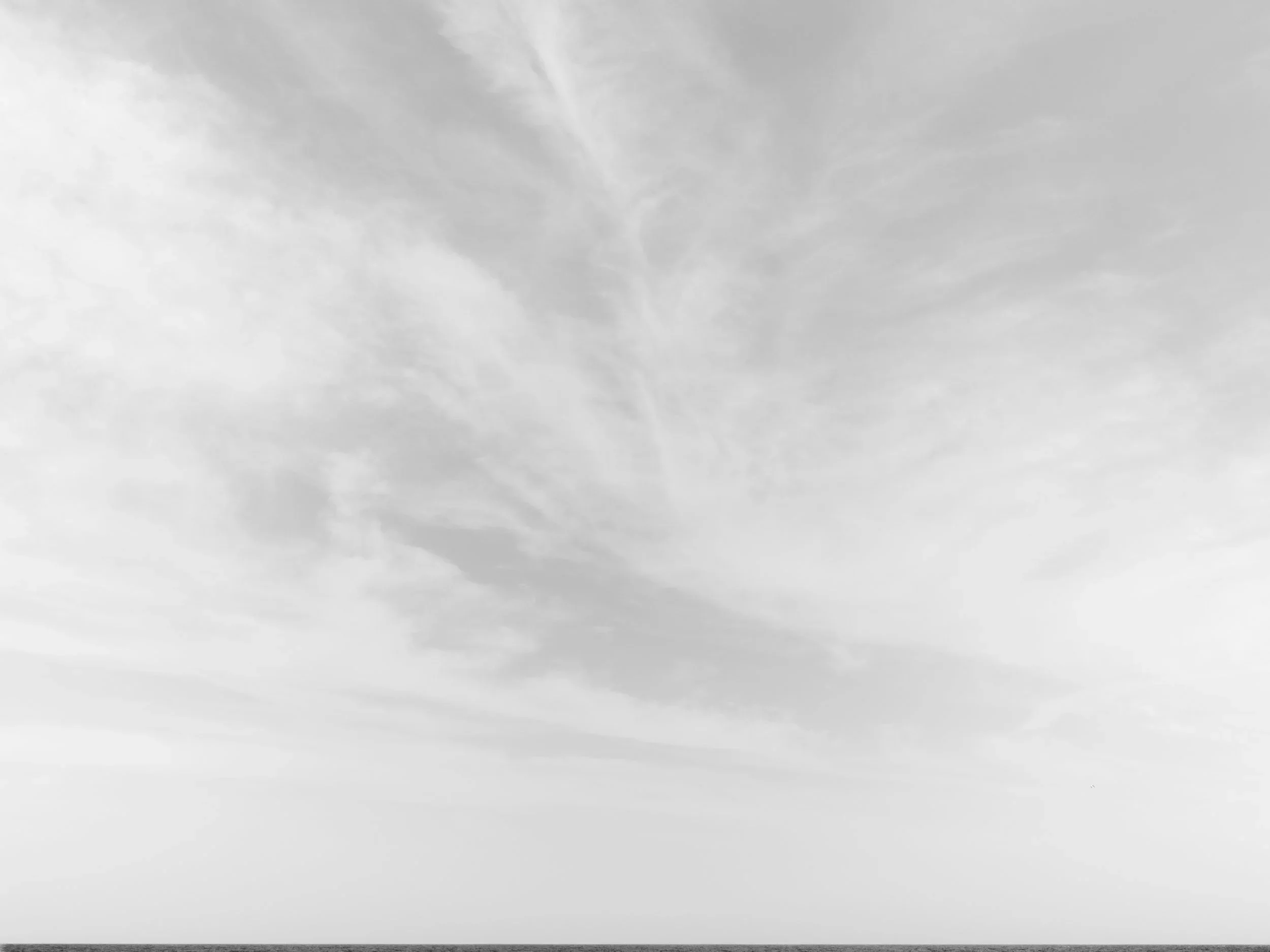 Black and white image of a cloudy sky over the ocean.