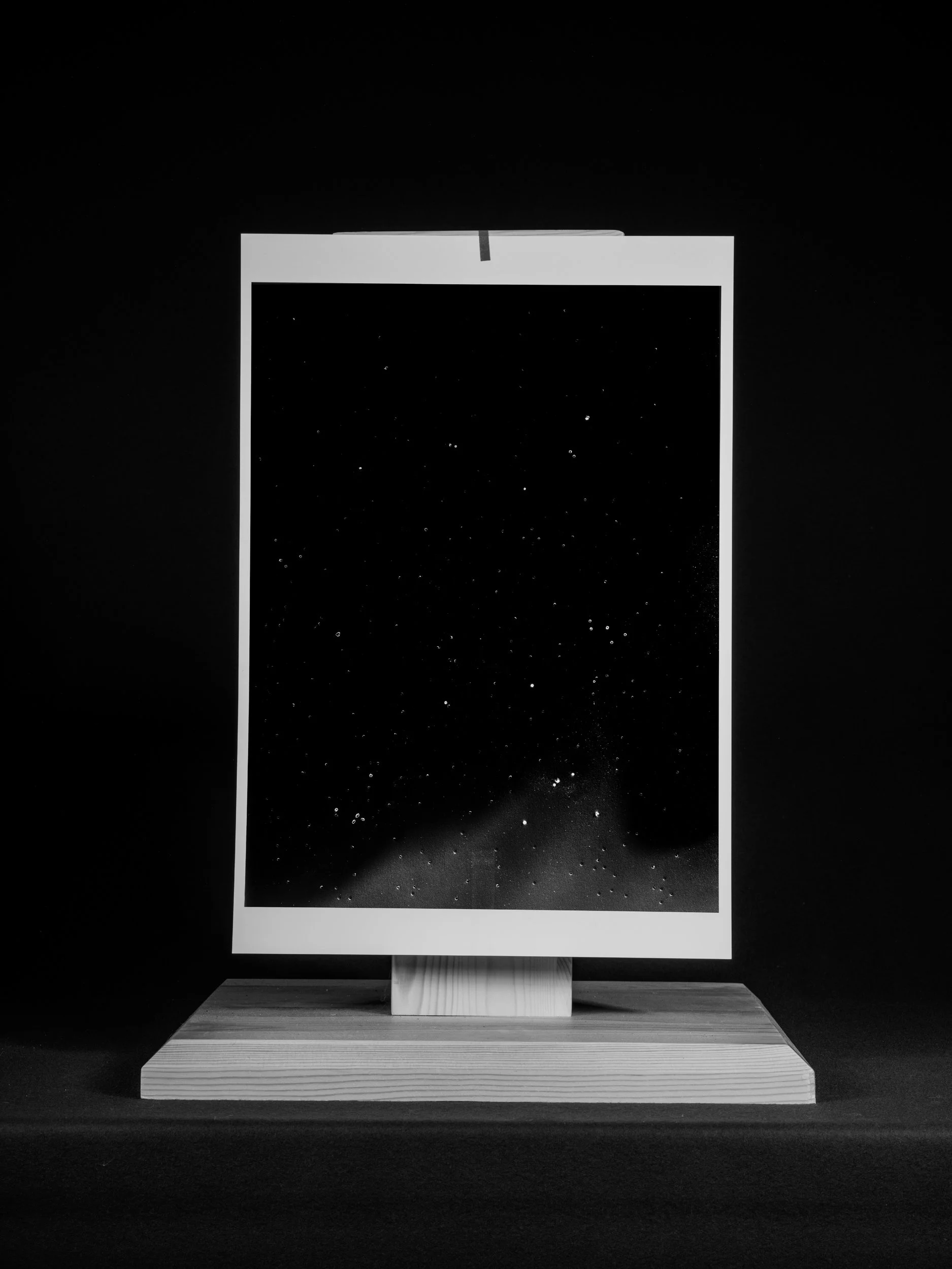 A black and white photograph of an art installation featuring a starry night sky image framed on a wooden stand.