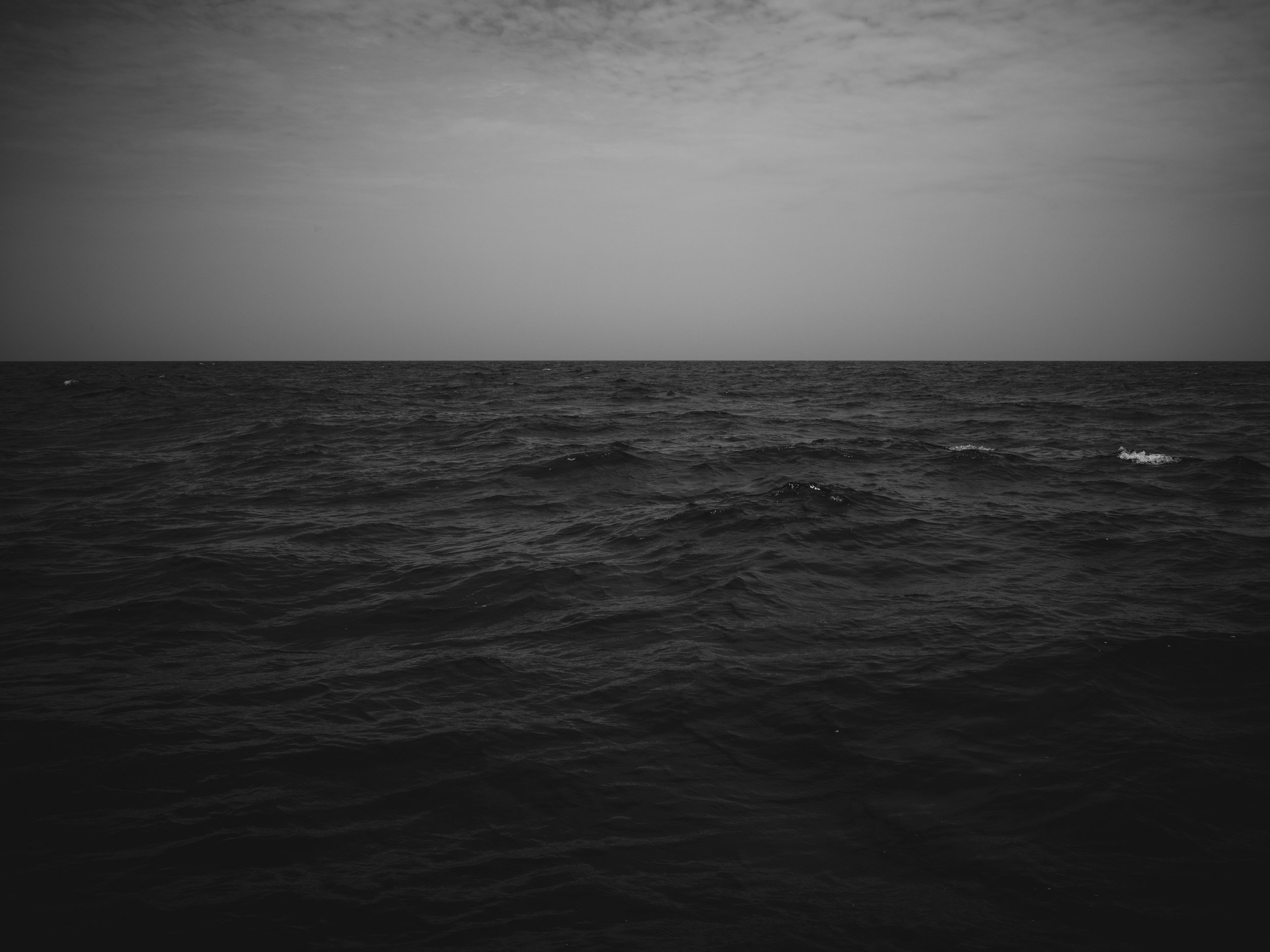 Black and white photo of the ocean's surface with waves, under a cloudy sky.