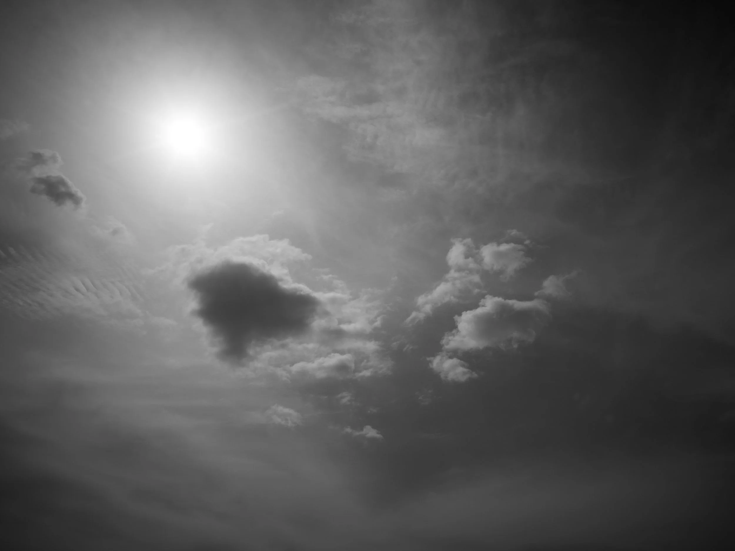A black and white image of a sky with clouds and a bright sun.