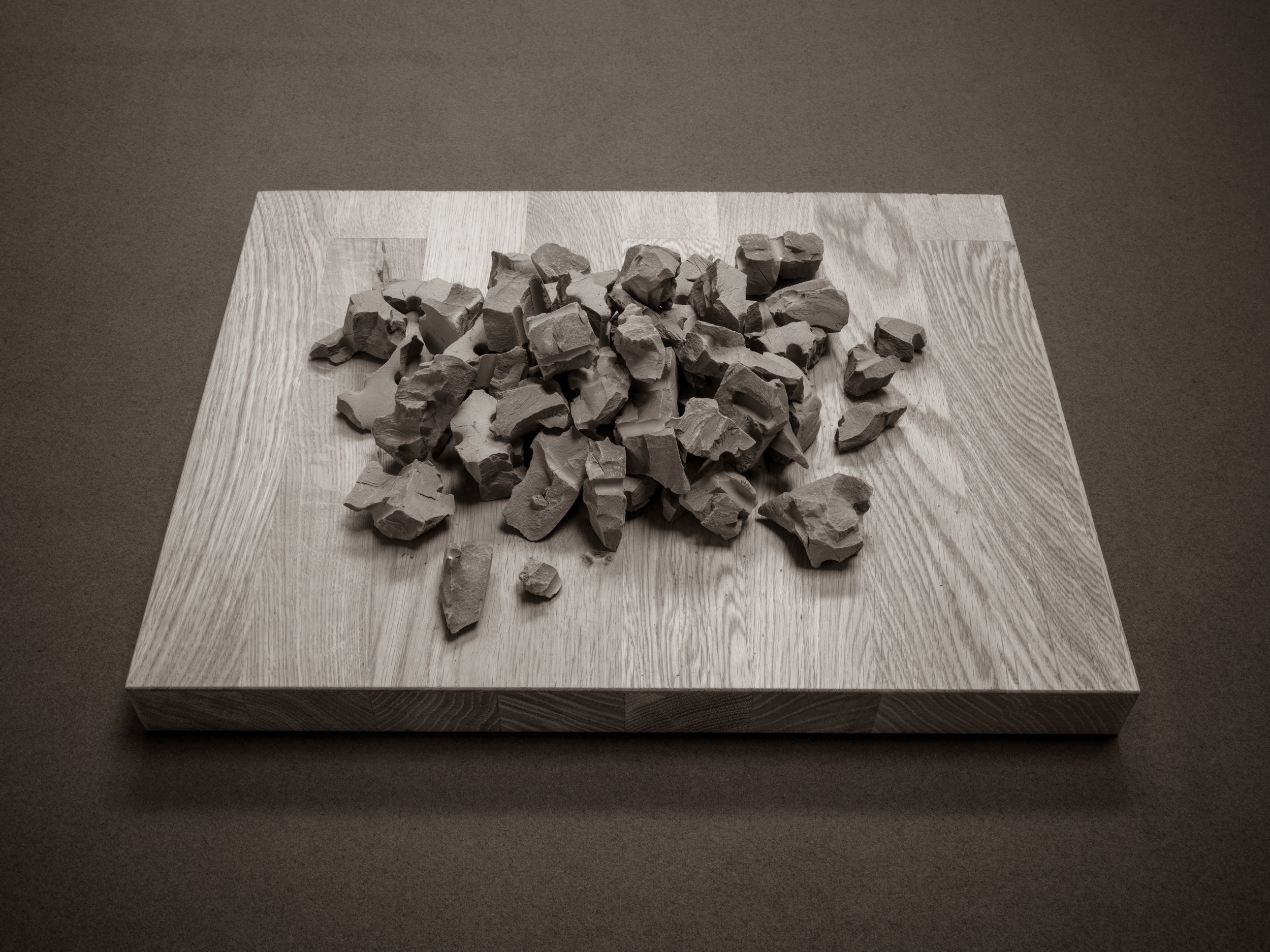 A square wooden table with a pile of broken rocks or clay pieces on it, set against a plain background.
