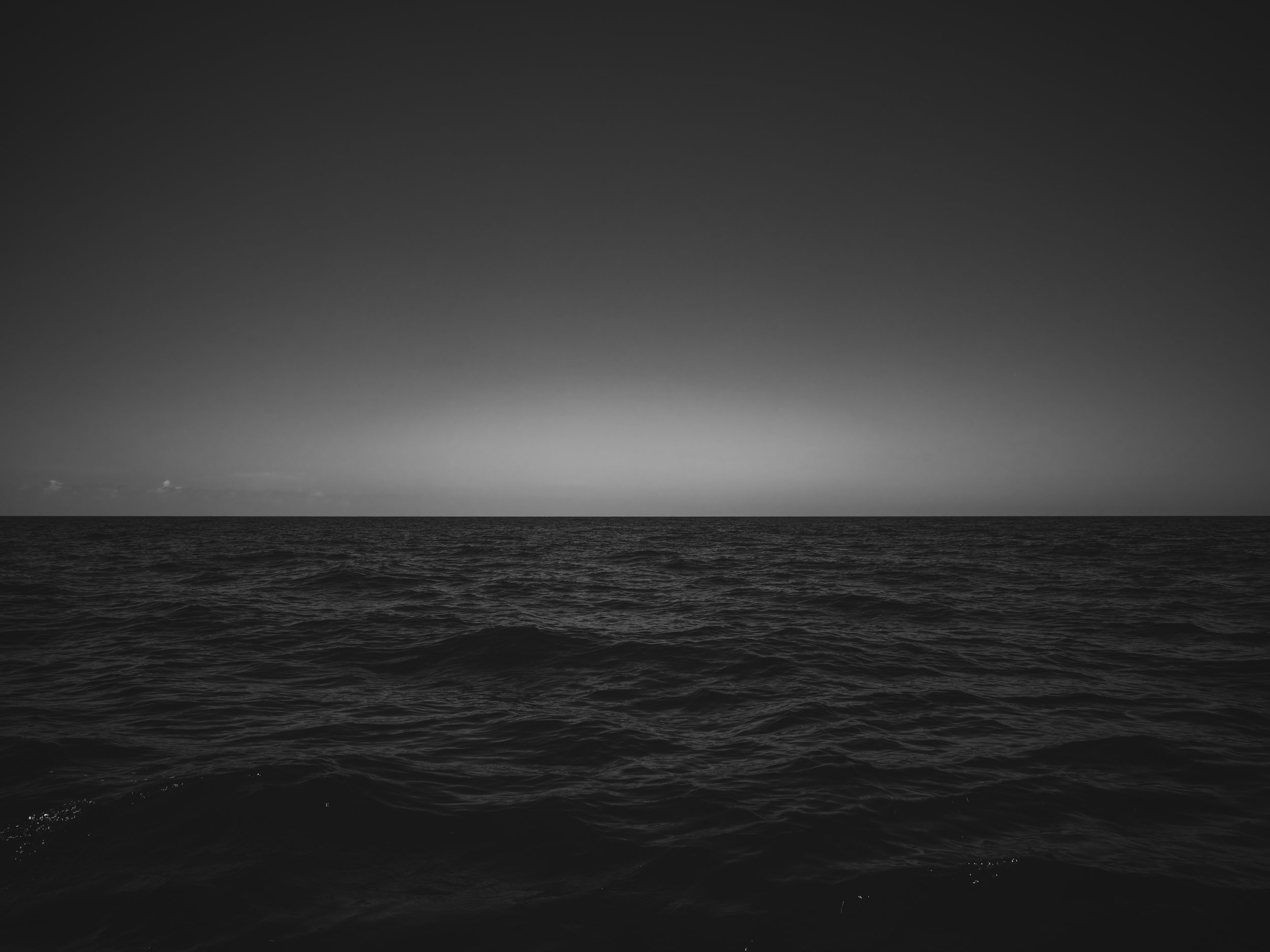 A black and white photo of the ocean with waves and a cloudy sky.