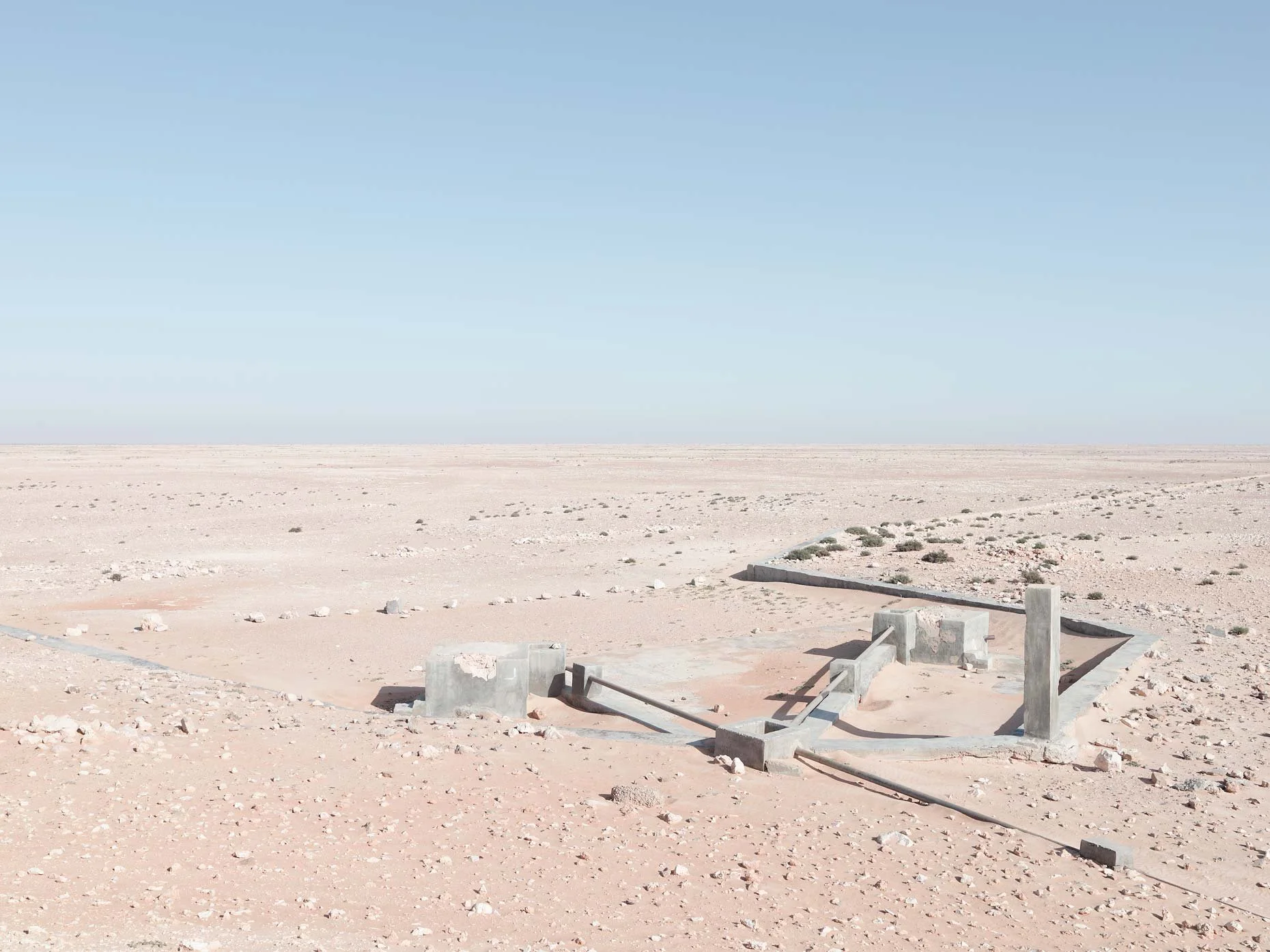 Desert landscape with sparse vegetation, concrete structures in the foreground, and a clear blue sky.
