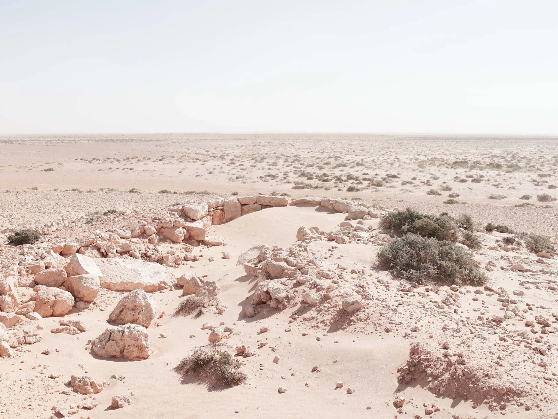 Desert landscape with rocky formations, sparse vegetation, and a clear sky.