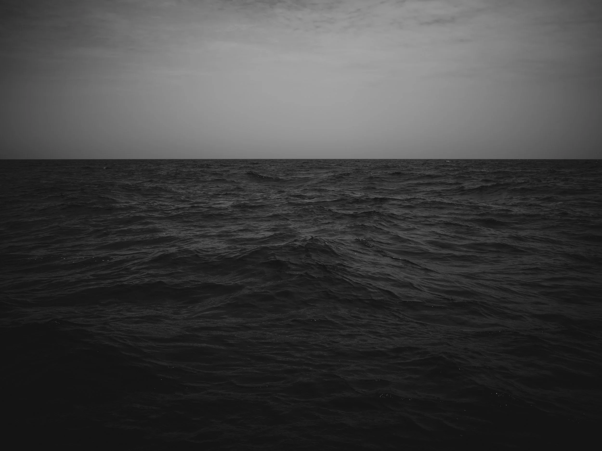 Black and white photograph of an ocean with a cloudy sky.
