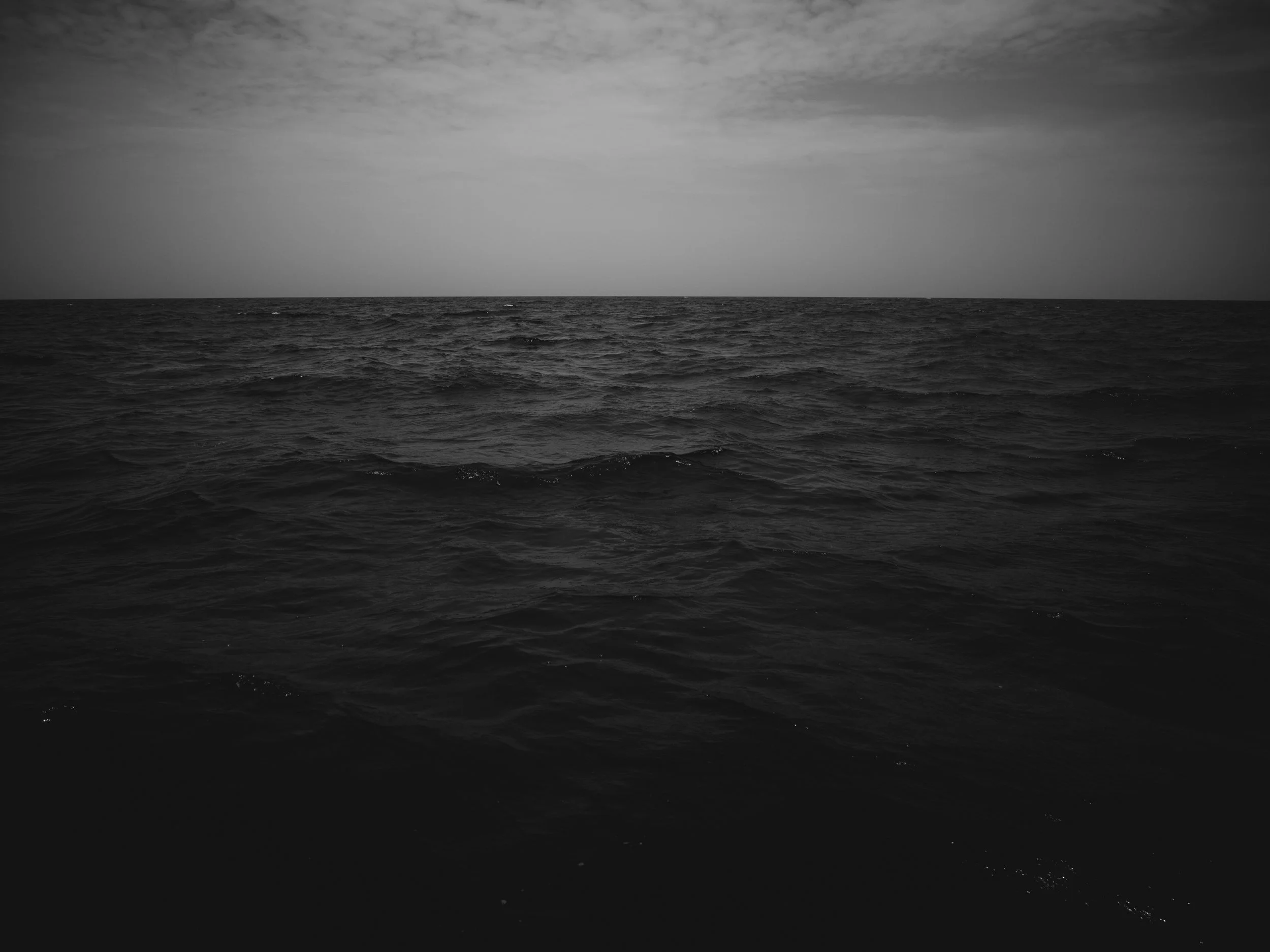Black and white photograph of the ocean with a horizon line and a cloudy sky.