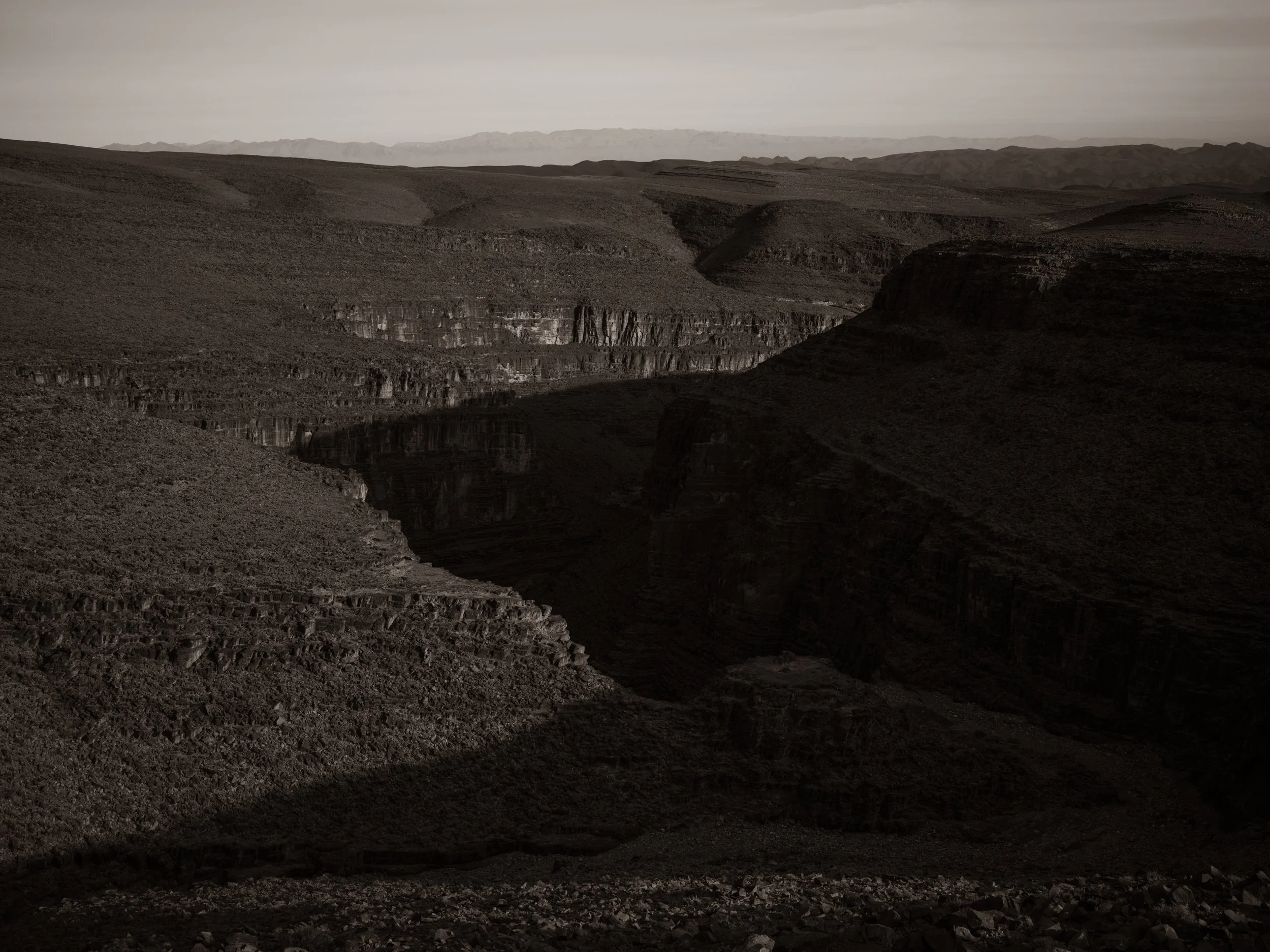 A vast desert landscape with rocky terrain and distant mountain ranges under a cloudy sky.