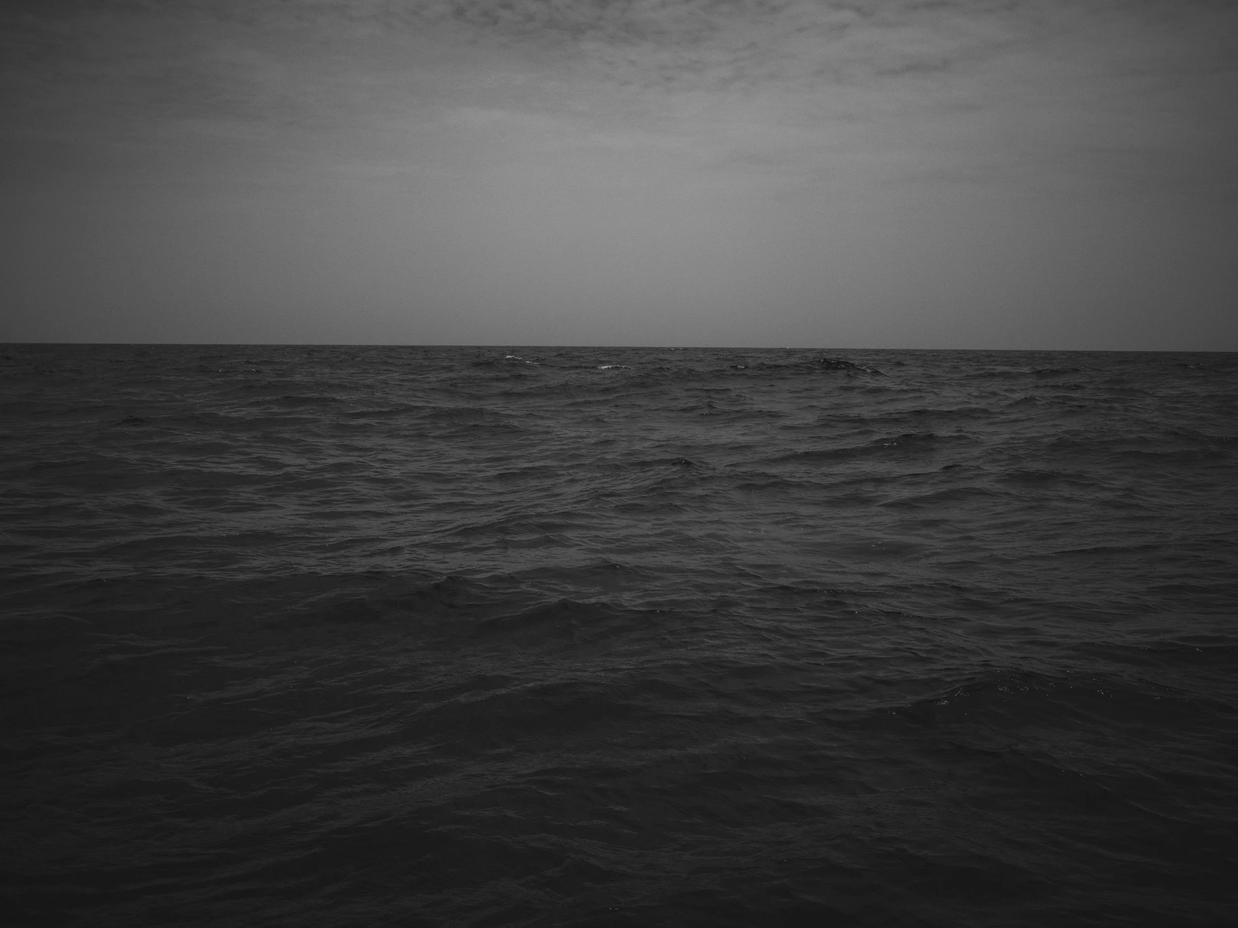 Black and white photo of the ocean with some clouds in the sky.