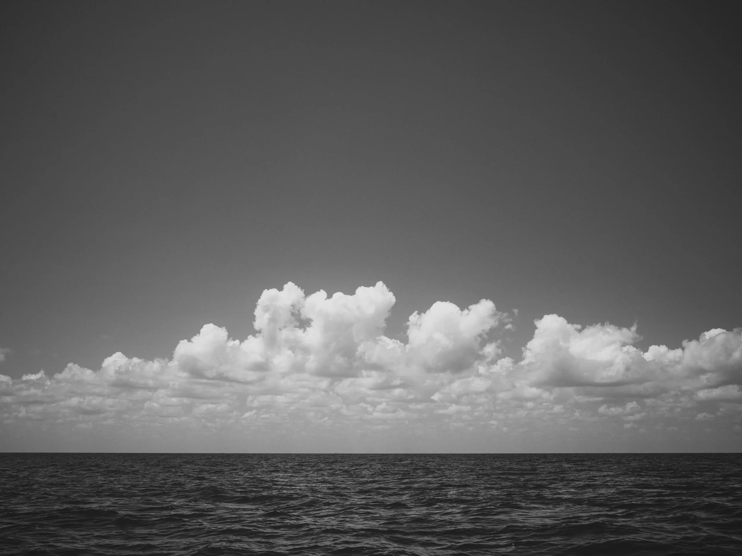 Black and white landscape photo of the ocean with a cloudy sky.
