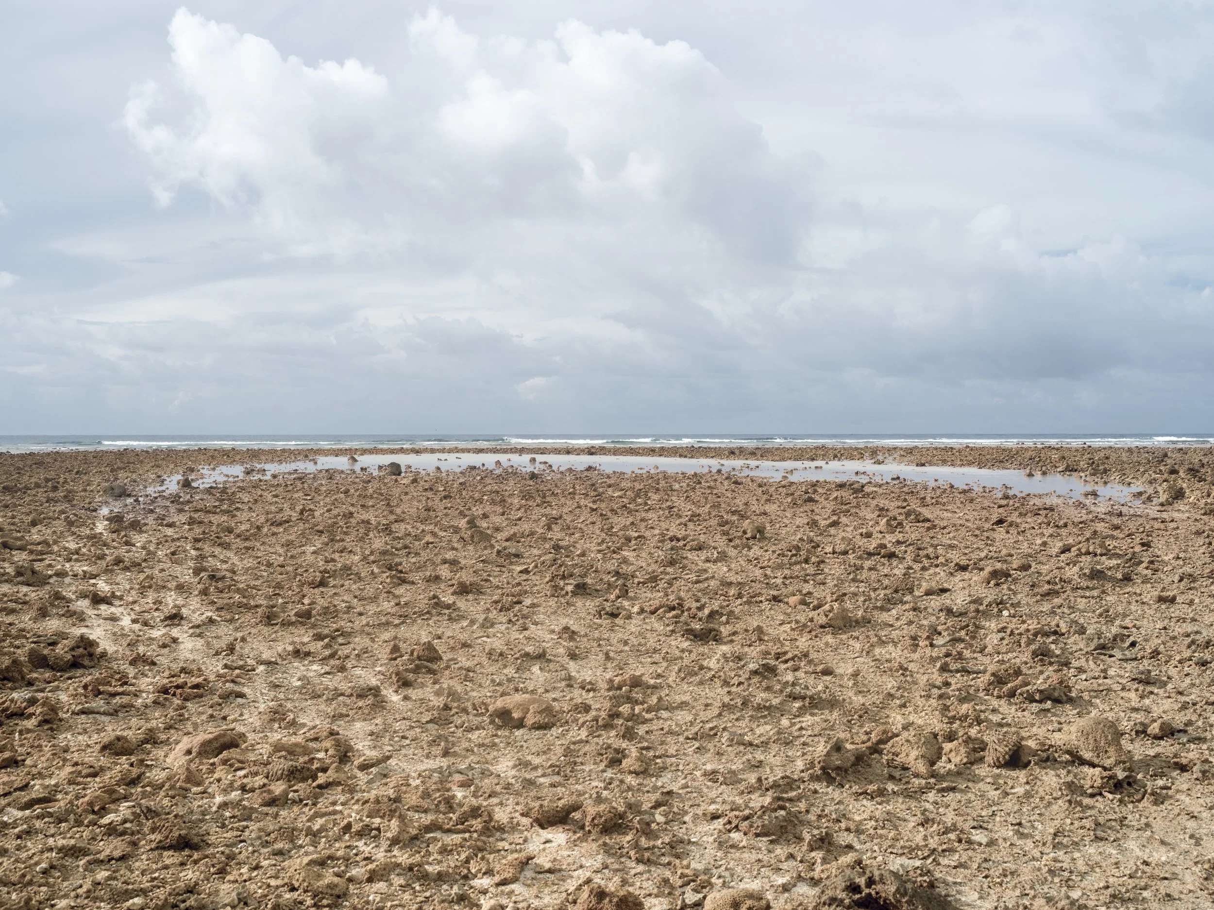 A rocky beach with small pools of water, ocean waves in the distance, and a partly cloudy sky.