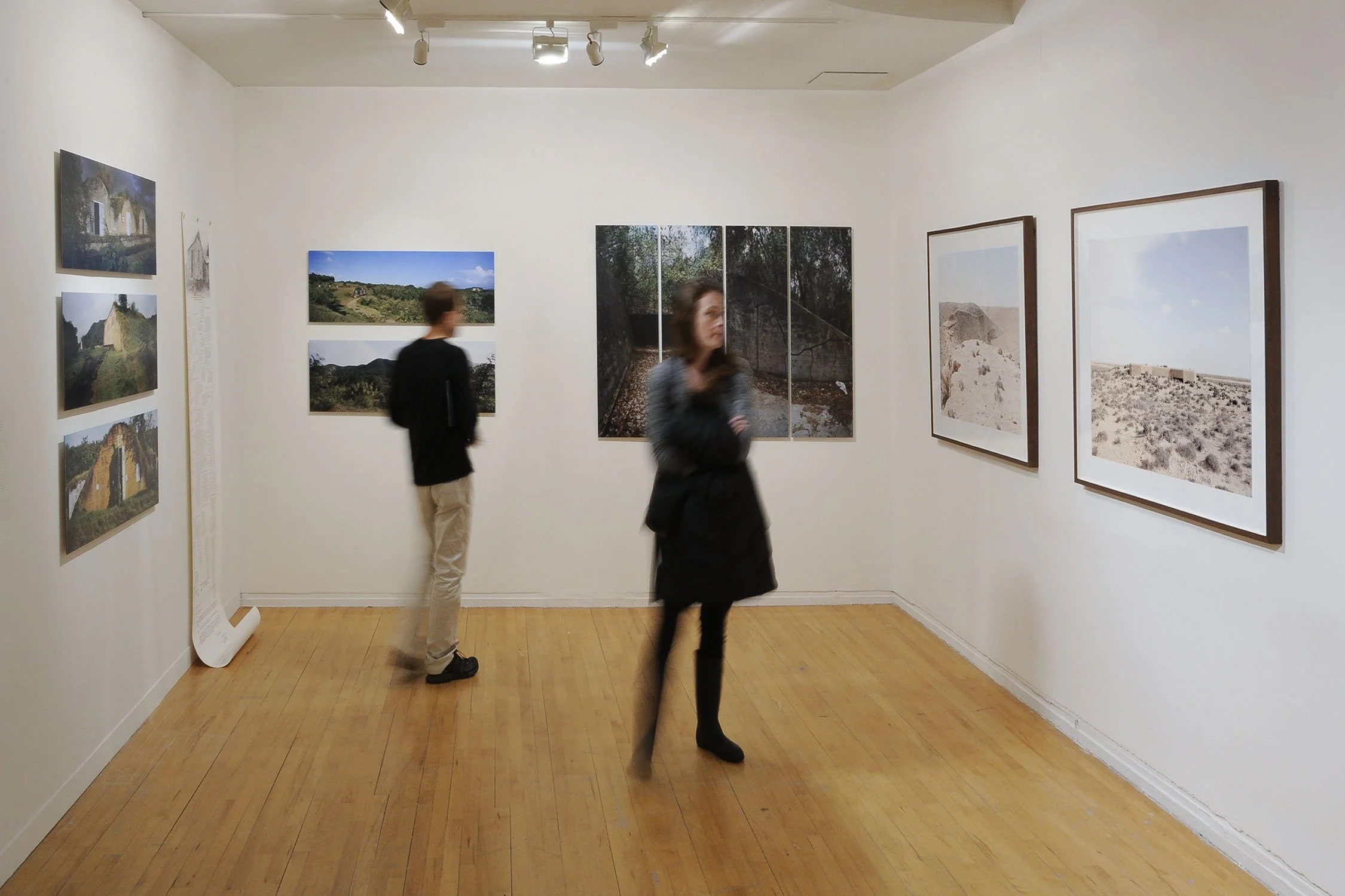 People viewing landscape photographs in an art gallery with white walls and wooden floors.