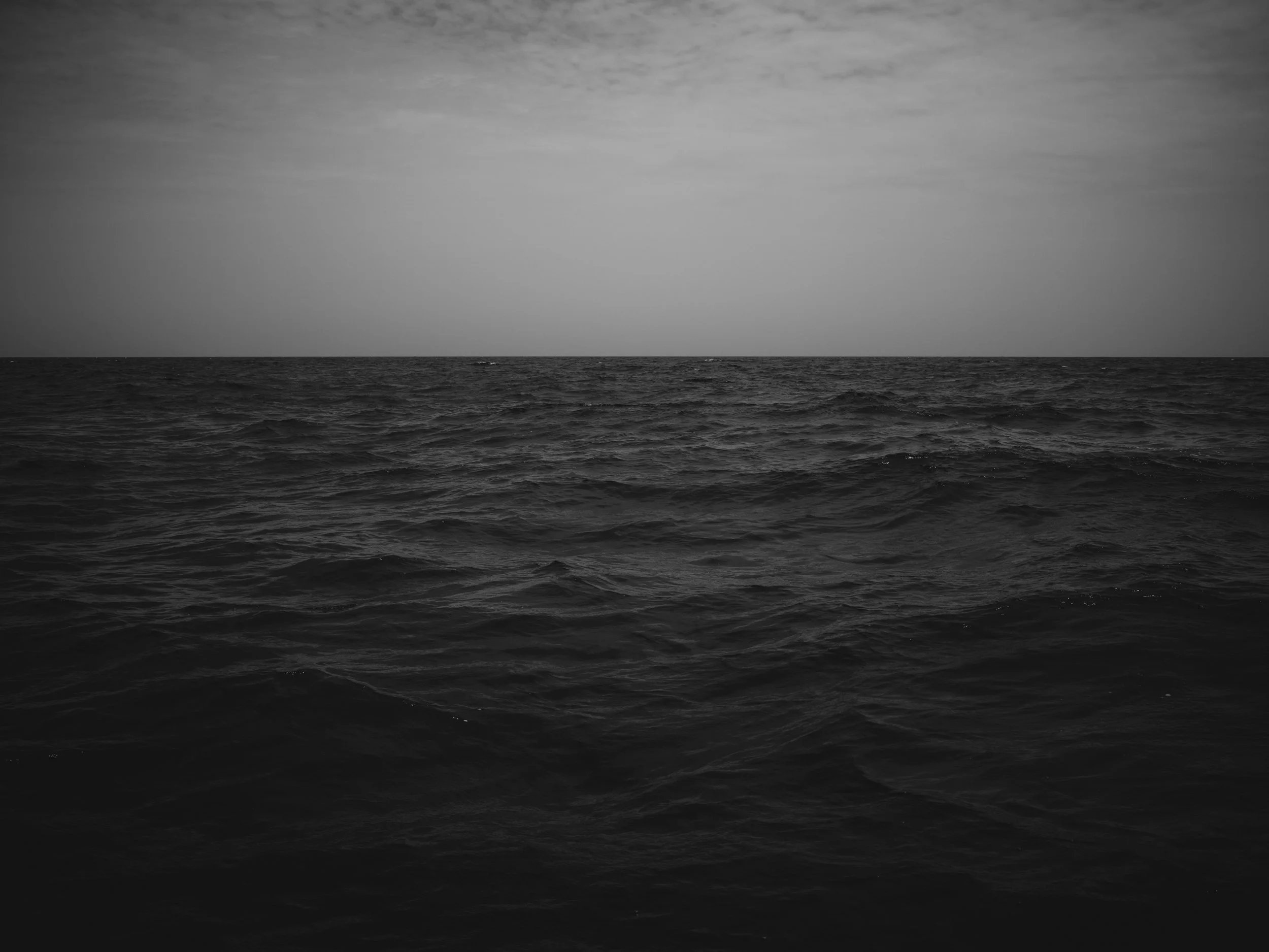 Black and white photo of the ocean with calm water and an overcast sky.