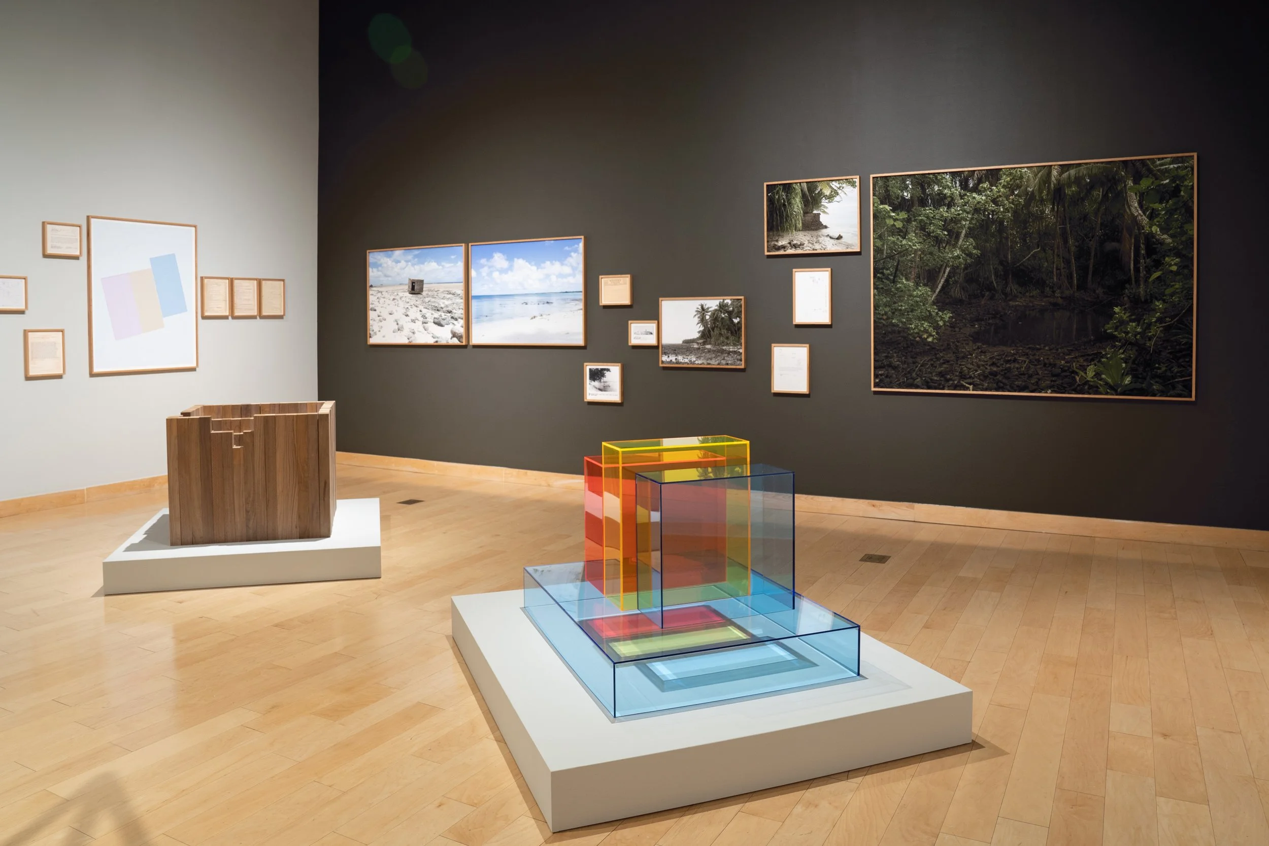 An art gallery displaying framed photographs of beaches and forests, with some colorful geometric sculptures in the foreground.