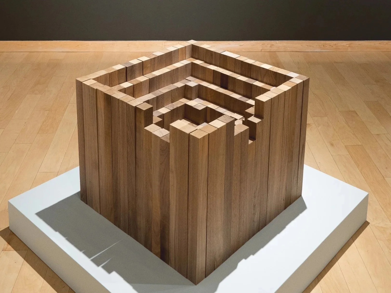 Wooden sculpture with nested rectangular frames inside a white platform.
