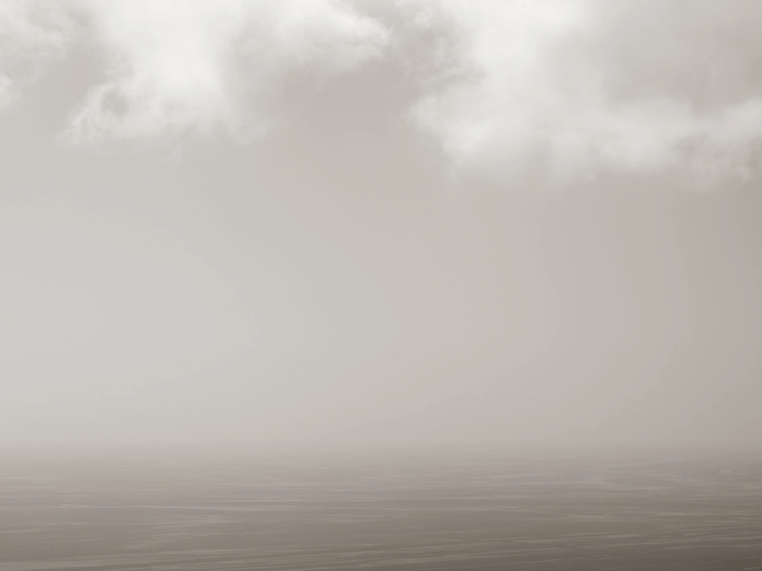 Overcast sky with gray clouds over a calm body of water, with a small strip of land in the distance.
