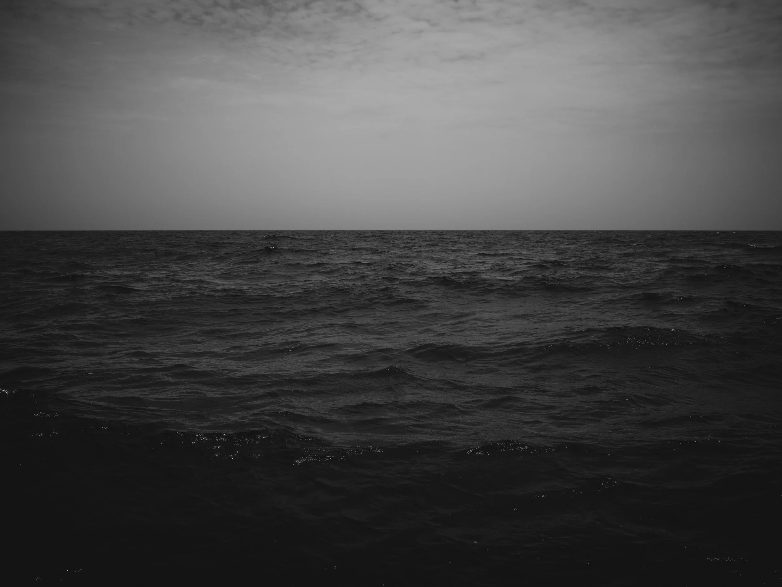 Black-and-white photo of the ocean with waves and a cloudy sky.